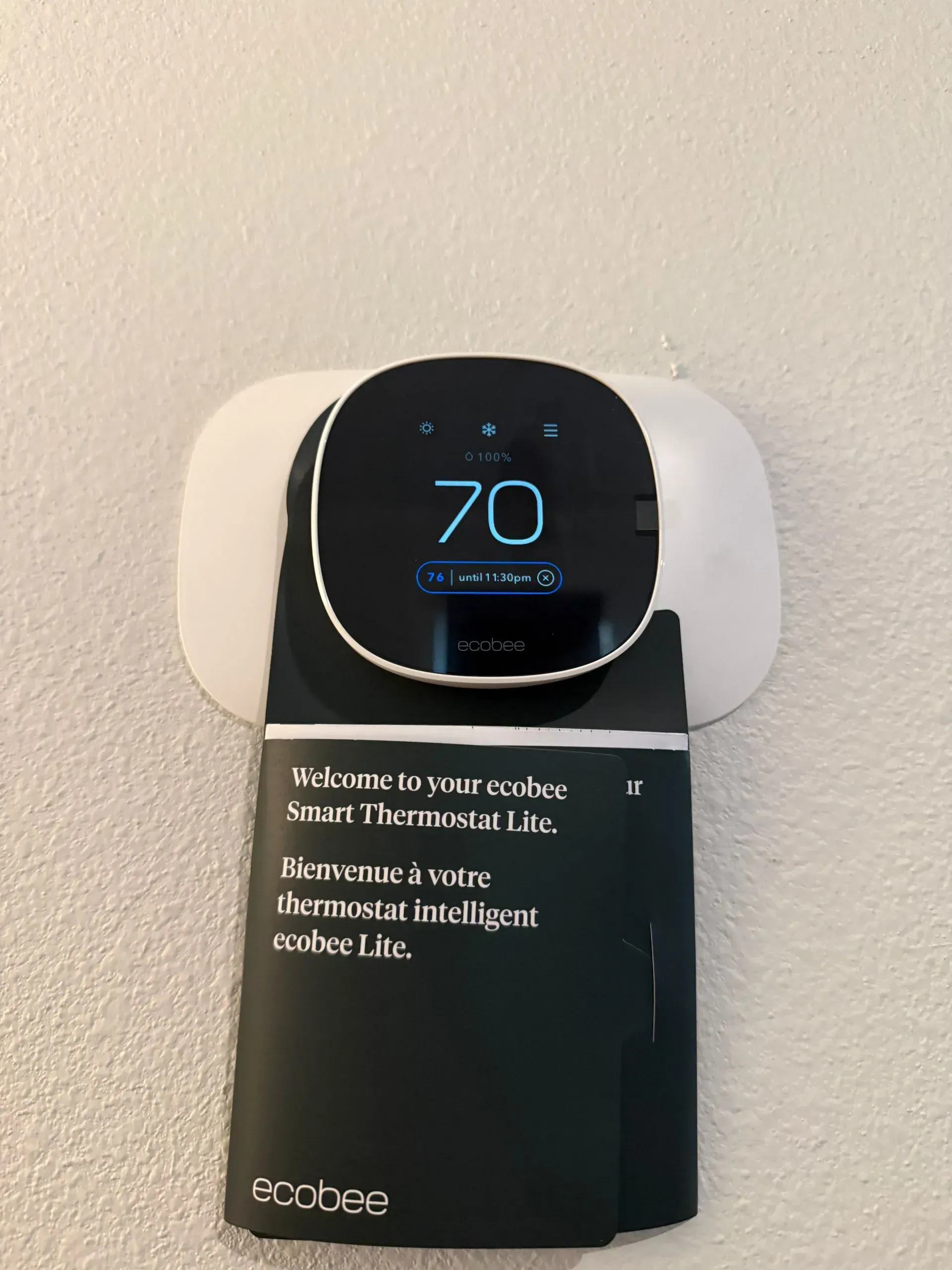 Black Ecobee thermostat showing 70° on a white wall with a welcome message on the screen