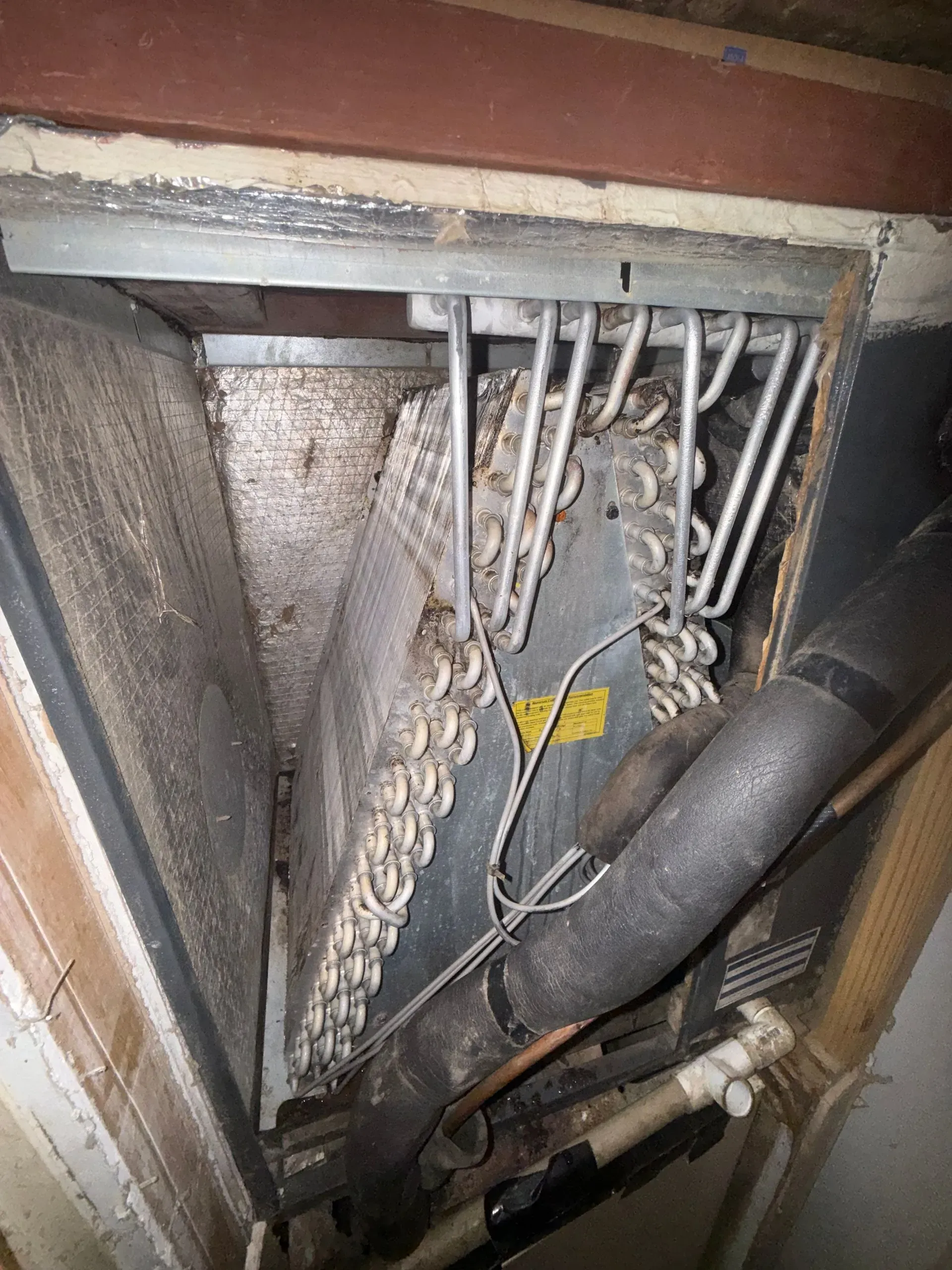 Close-up of HVAC unit interior with copper tubing, fins, and wiring, showing dust and wear