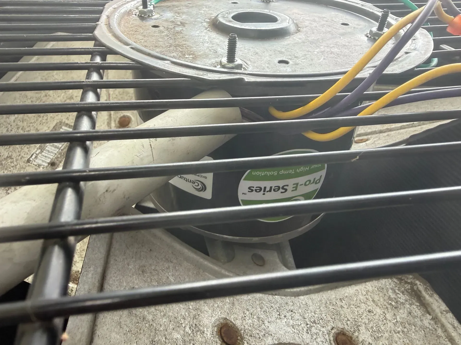 Close-up of a metal fan motor with wires behind black safety bars, resting on a concrete surface