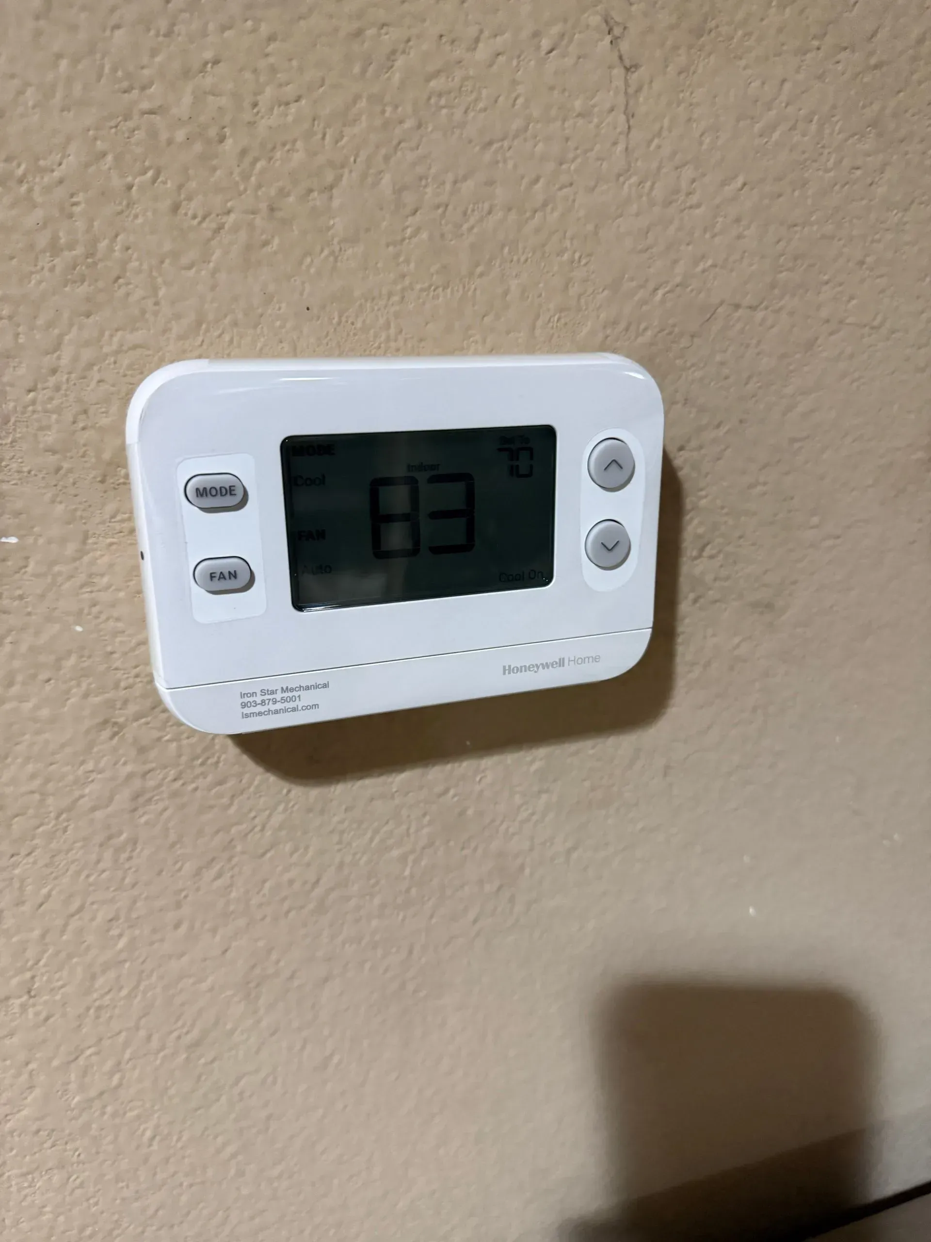 White wall thermostat displaying 83°F on a beige wall