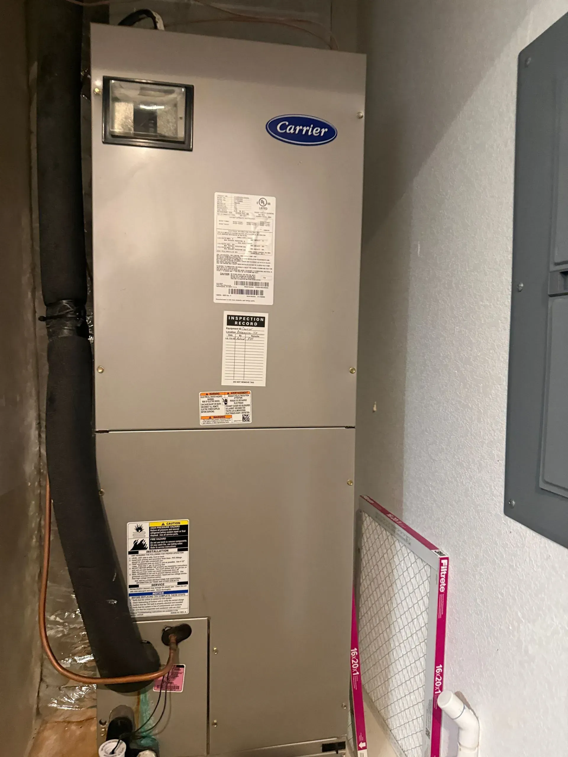 Tall gray furnace in a narrow utility closet with exposed vent pipe and wall panel.