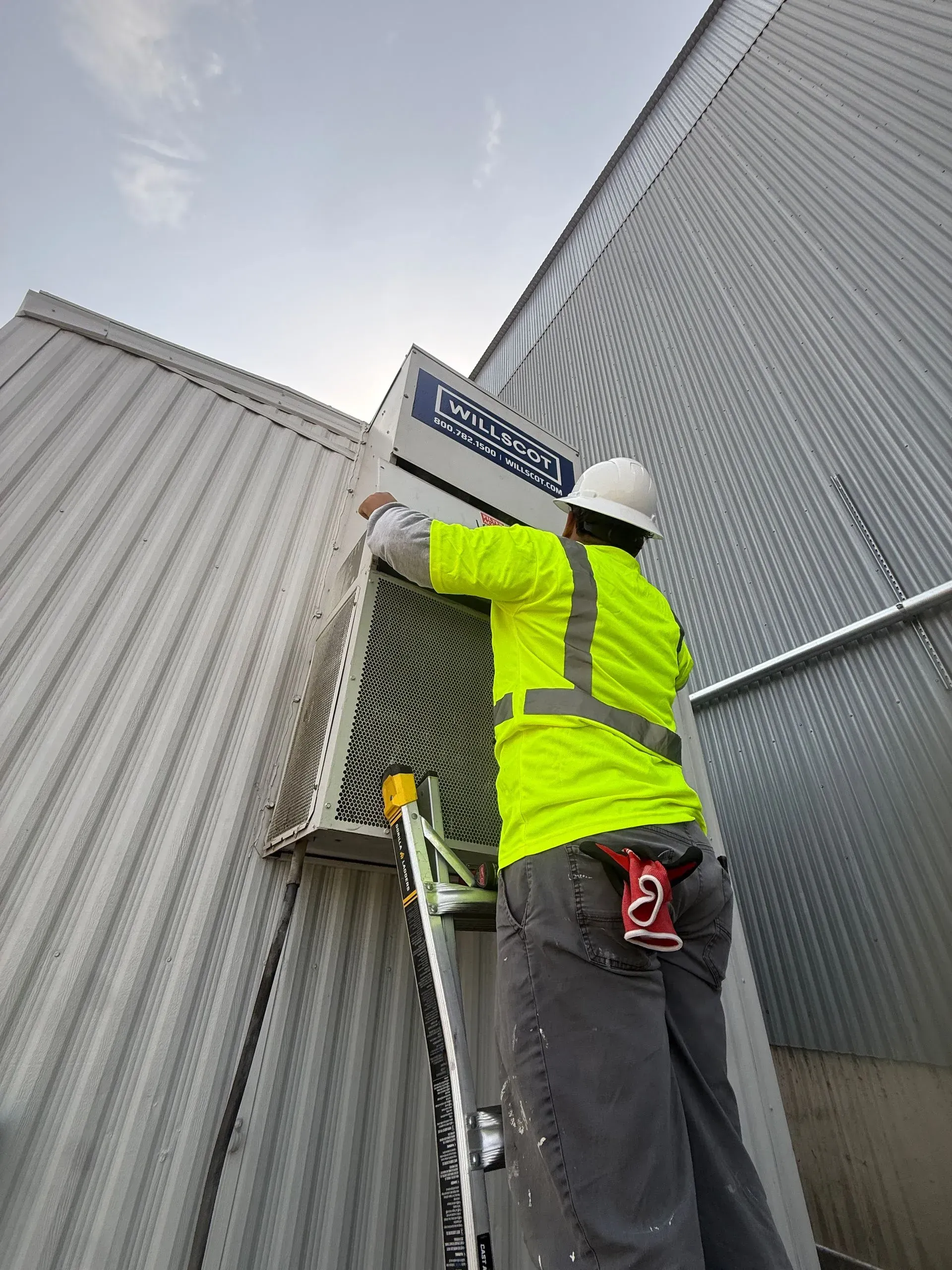 Worker in neon safety vest and hard hat adjusting a sign on a corrugated metal building.