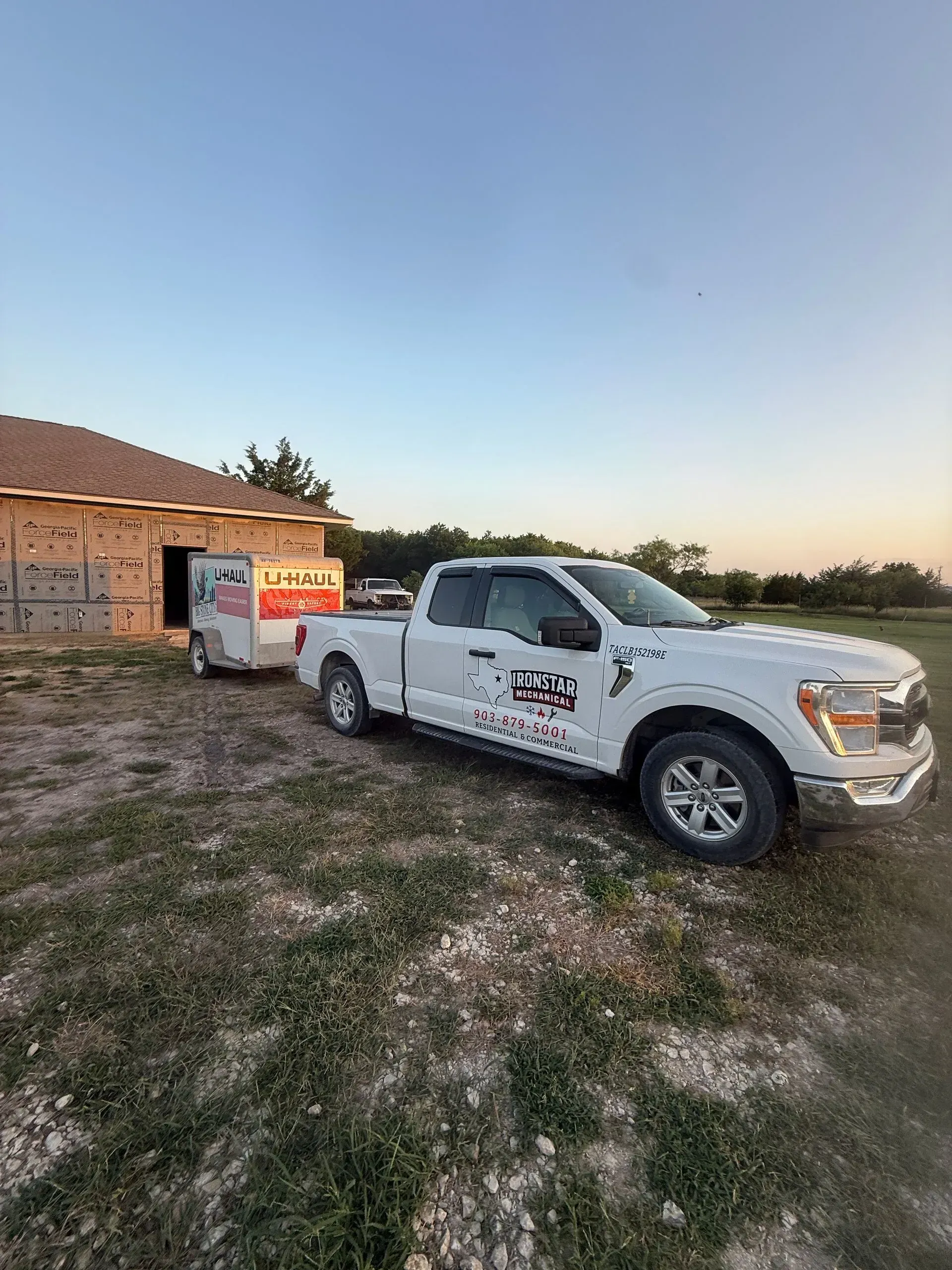 White pickup truck parked on a dirt lot beside a small building at sunset