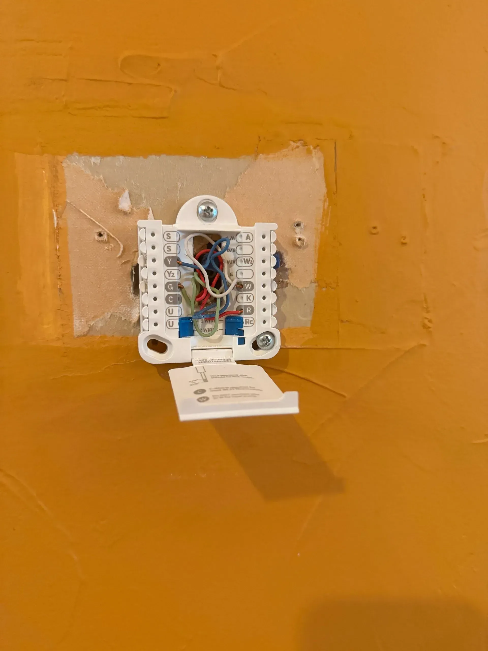 Open electrical wiring box on an orange wall with tape around it