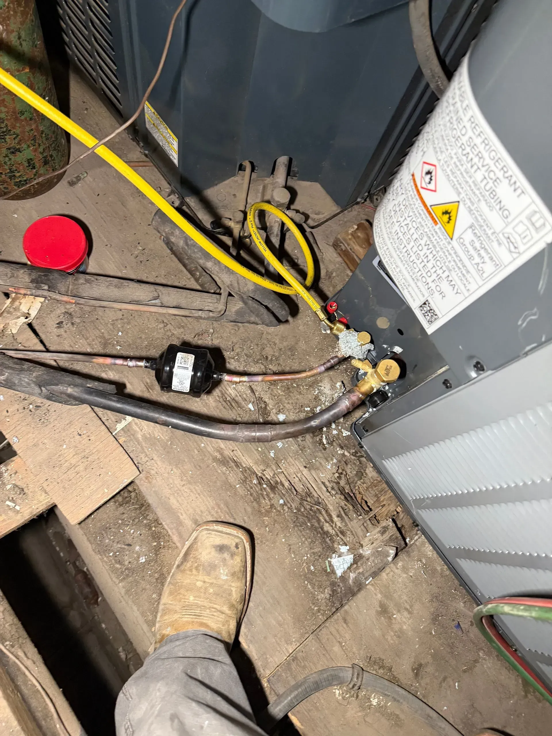 Dirty utility area with HVAC unit, tangled cables, and a worker’s boot visible on the floor