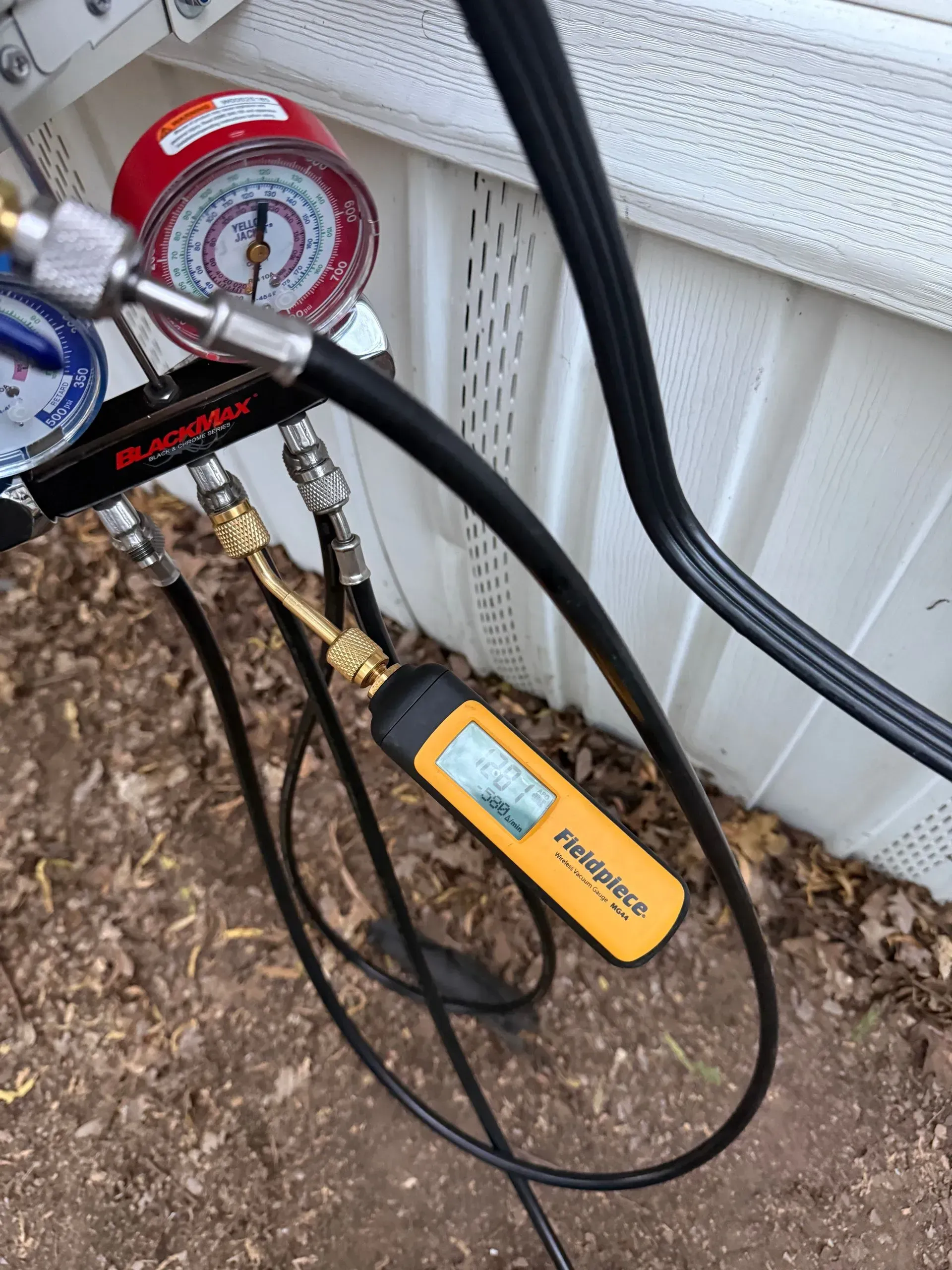 Pressure gauge and hoses connected to a yellow handheld device on a dirt surface outdoors