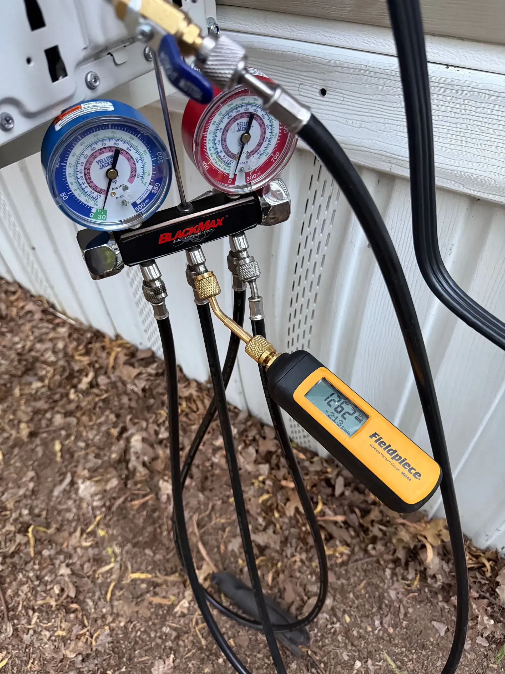 HVAC manifold gauges connected to hoses and a yellow digital thermometer on an outdoor unit