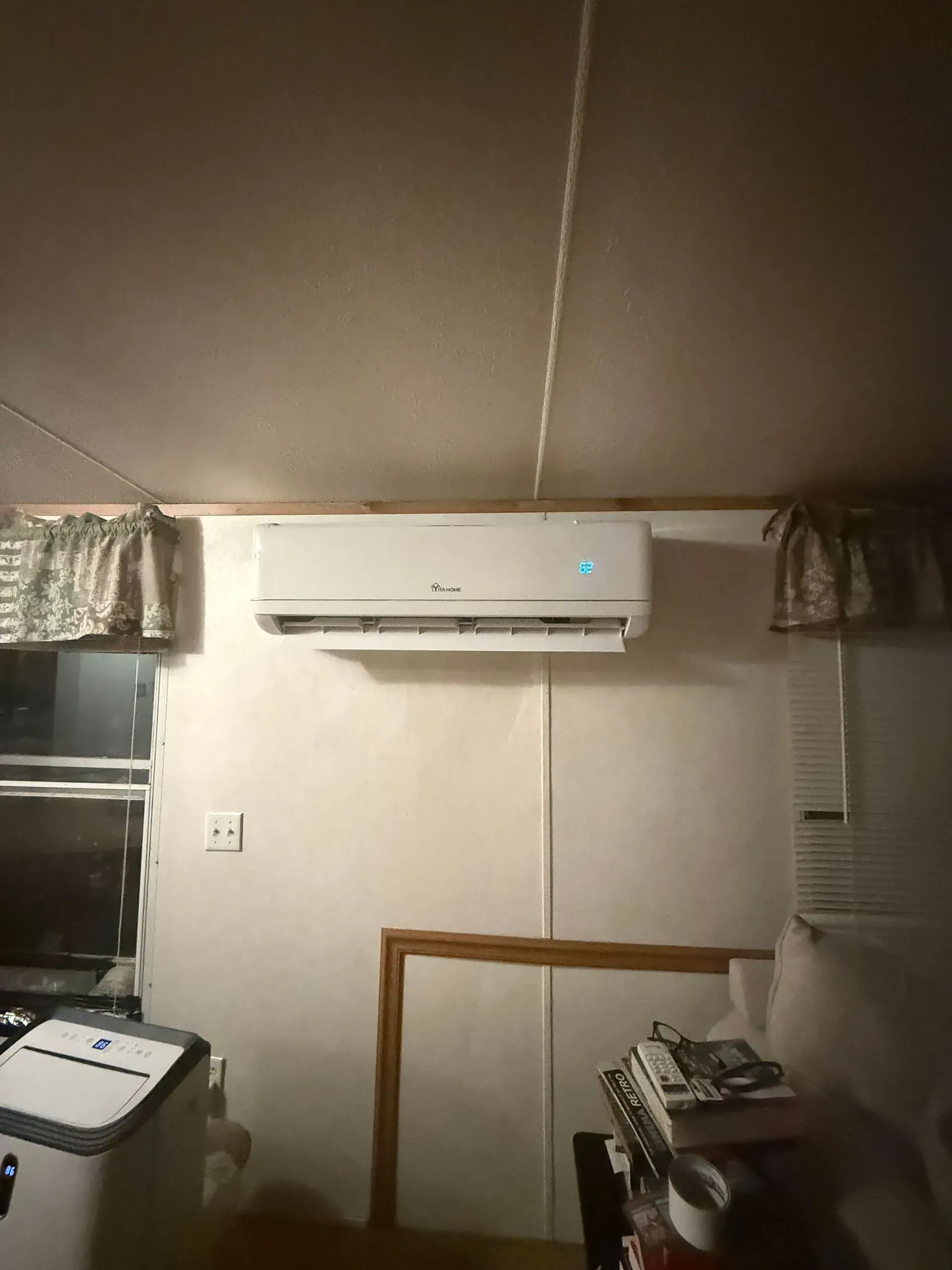 Small room with a wall-mounted air conditioner above a window and furniture below.