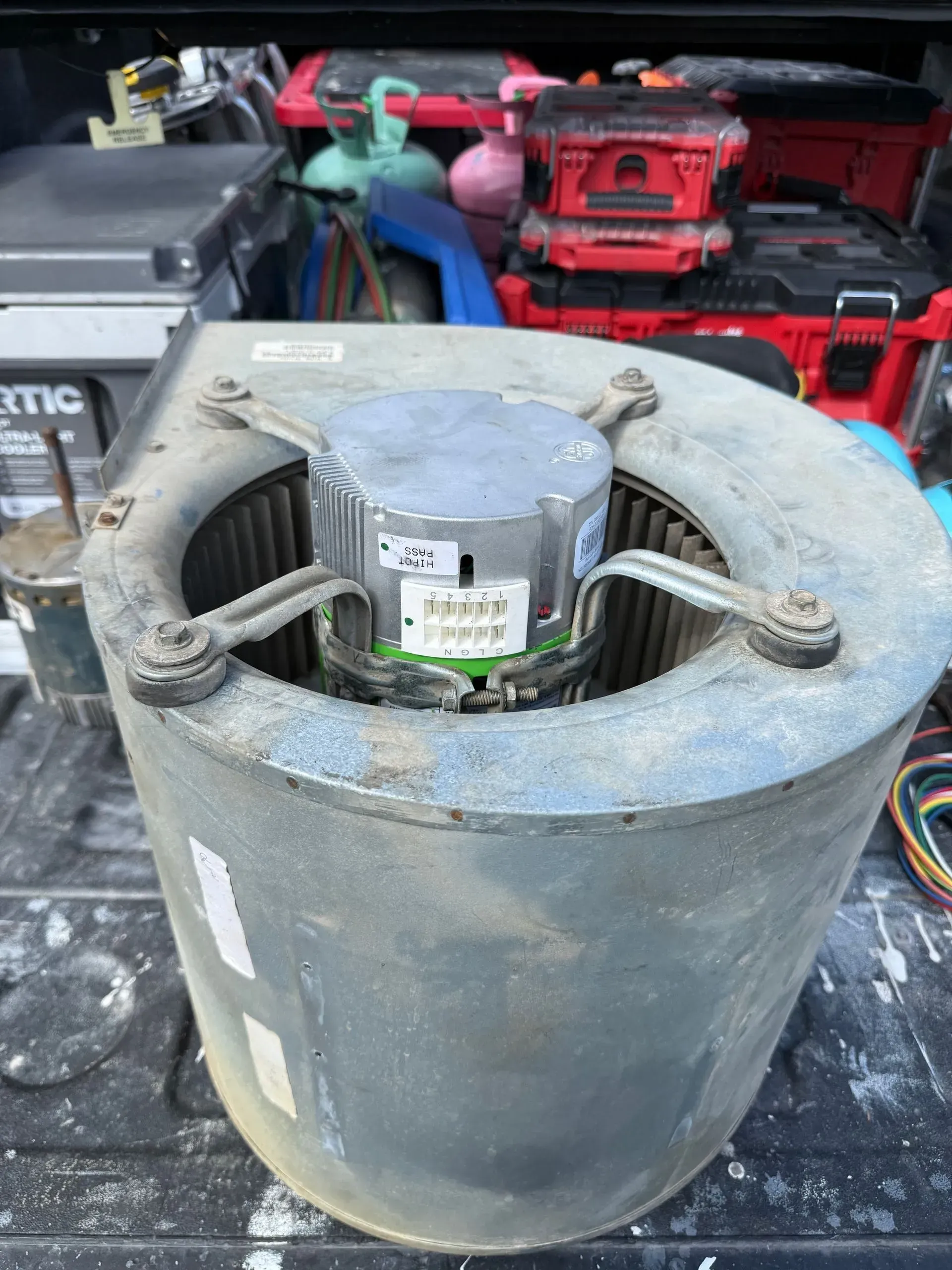Dusty gray industrial blower motor on a workbench, with tools and red cases in the background