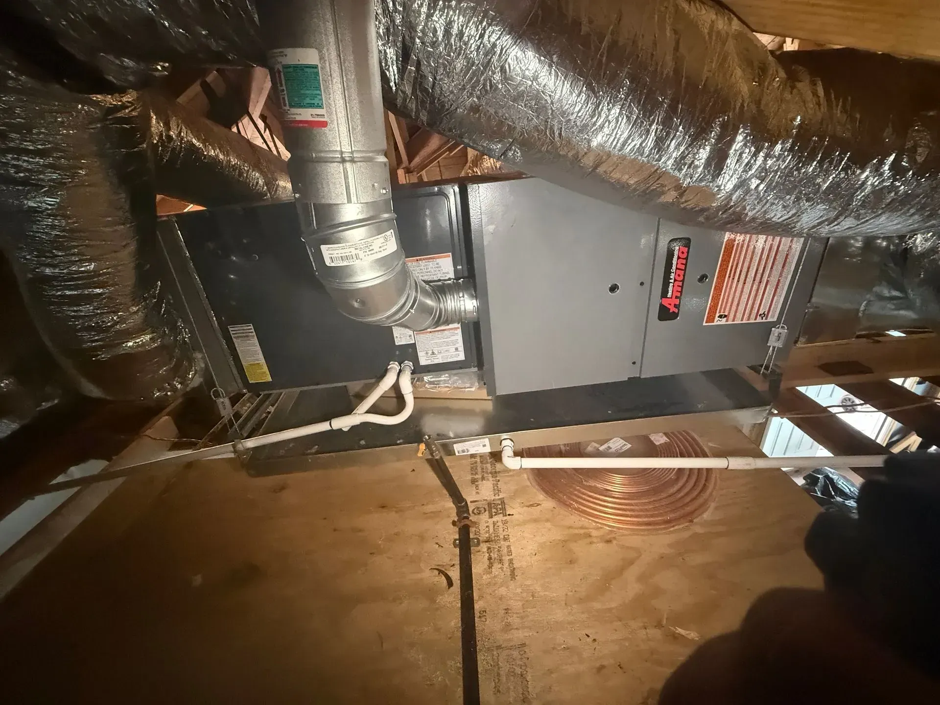 Crawl space with HVAC unit, shiny ductwork, and insulation under a wooden floor