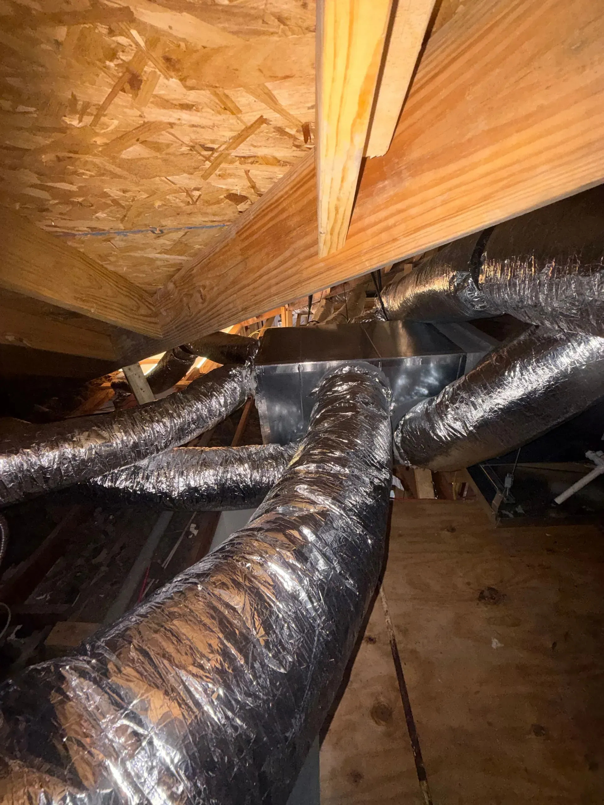 Attic ductwork beneath wooden roof framing with insulated flexible air ducts