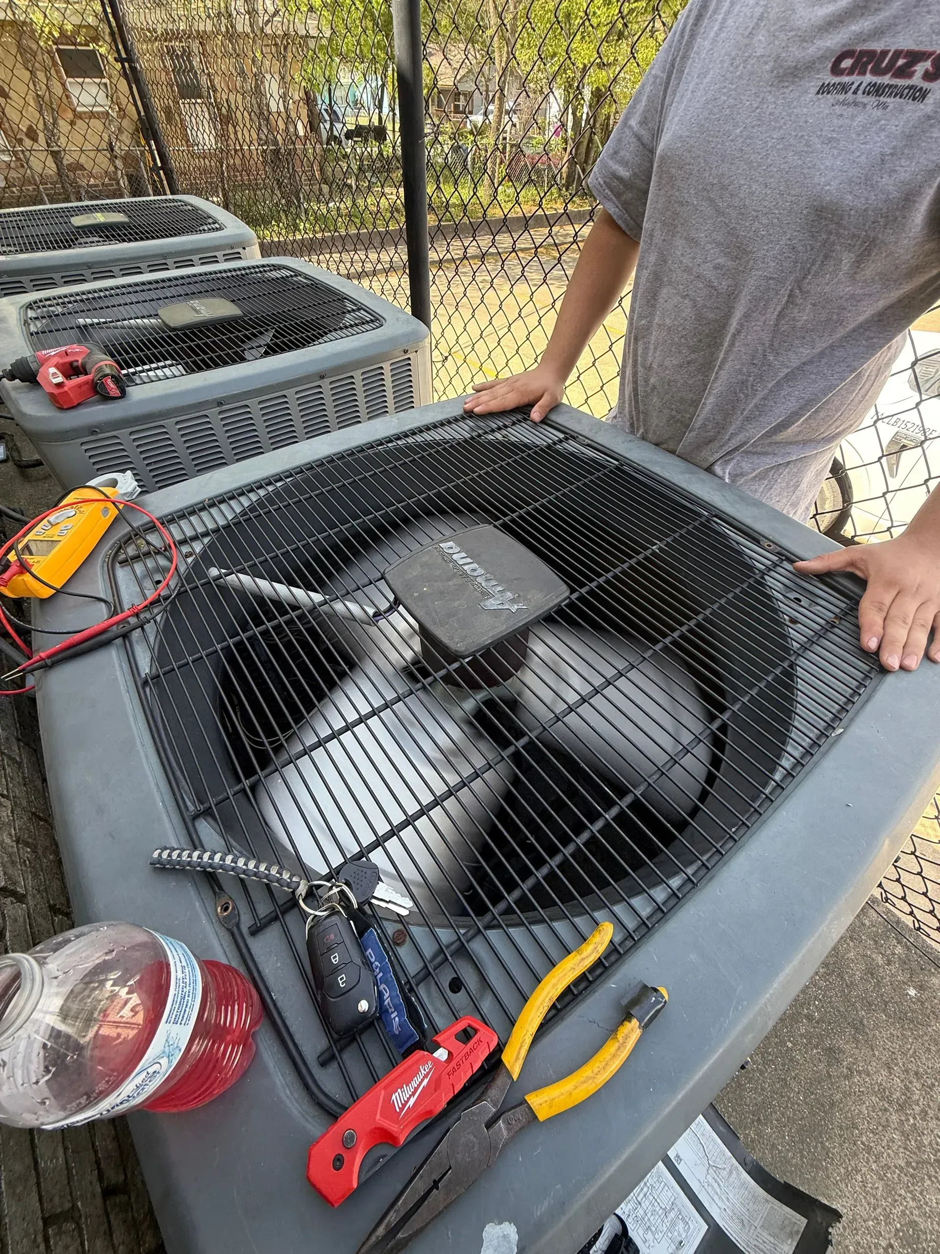 Person beside a large outdoor fan, with tools and equipment on a table in a yard