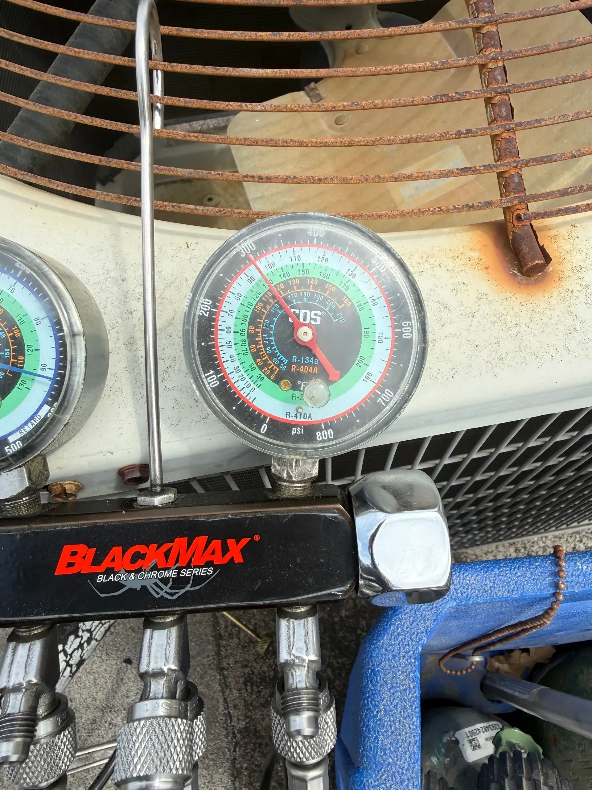 Air conditioner gauges on a BlackMax manifold, with hoses and the unit’s fan grille behind them
