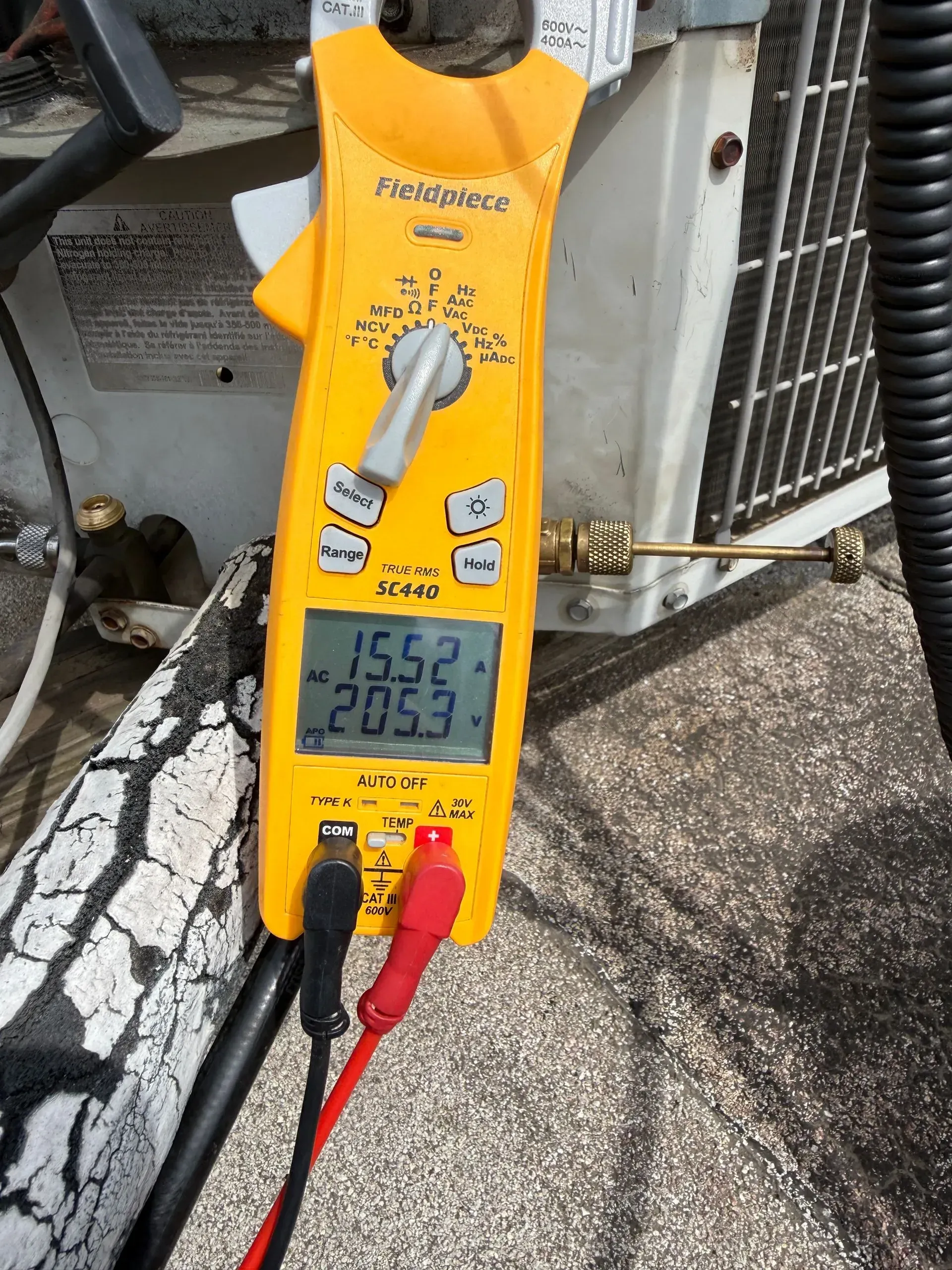 Yellow digital clamp meter with red and black probes showing a reading on a pavement.