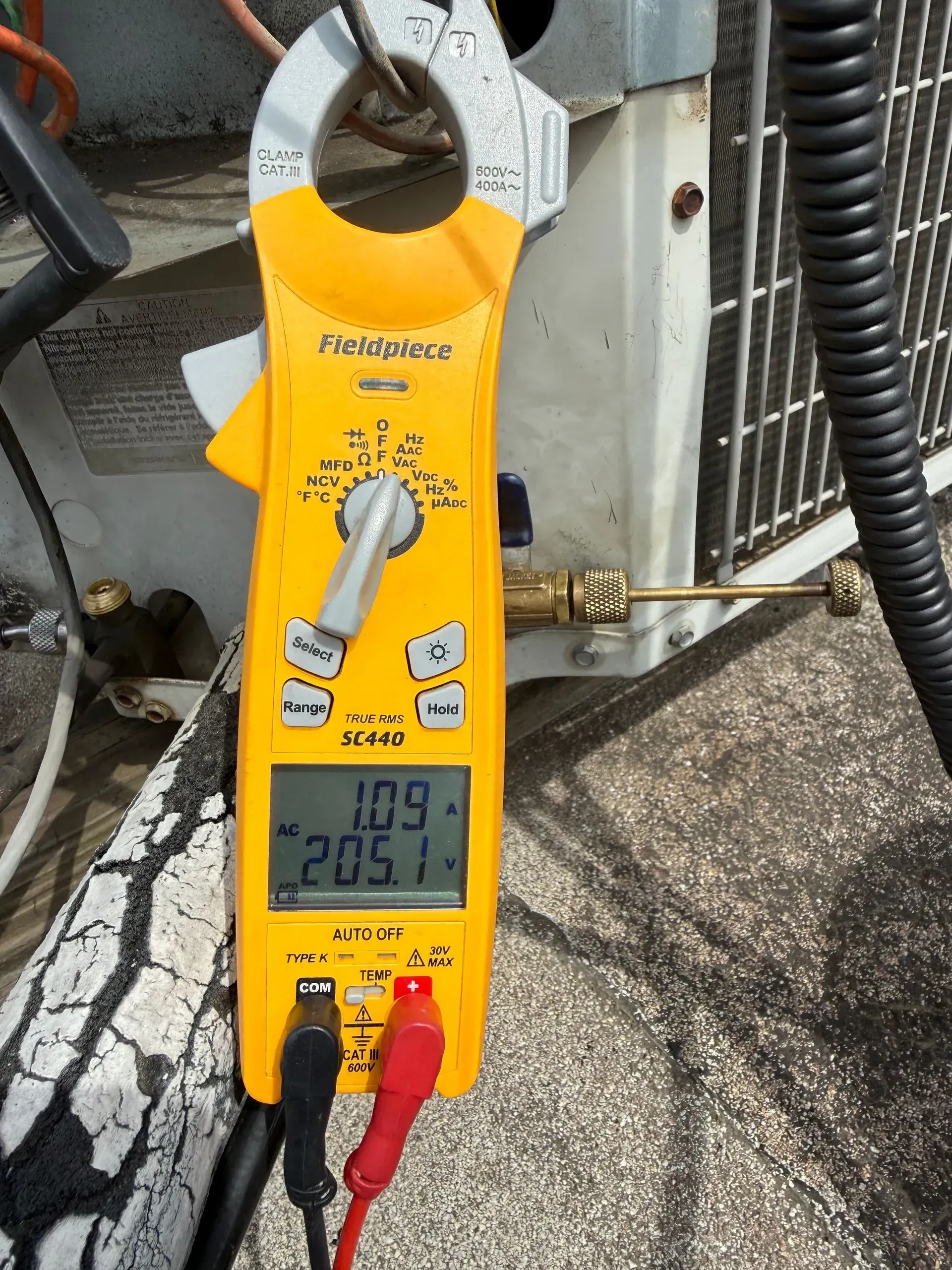 Yellow clamp multimeter measuring electrical current, displaying 11.9 and 205.1 on a rooftop conduit.
