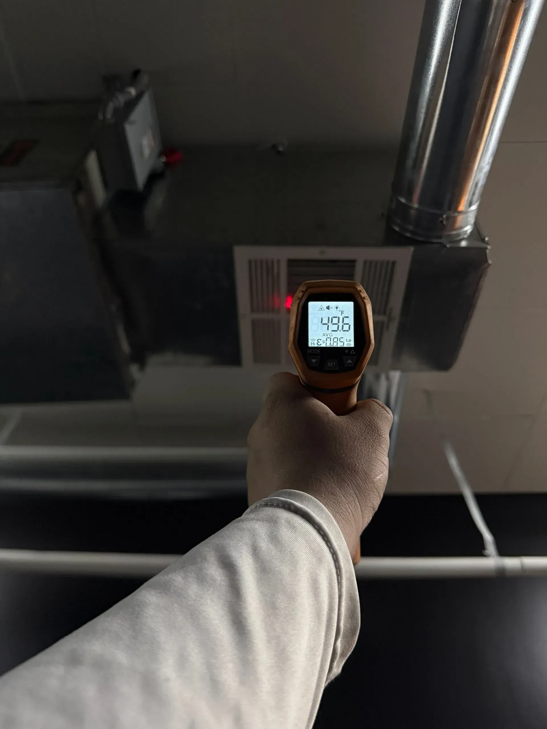Hand holding a thermal camera aimed at a ceiling vent, showing a 9.6° reading.