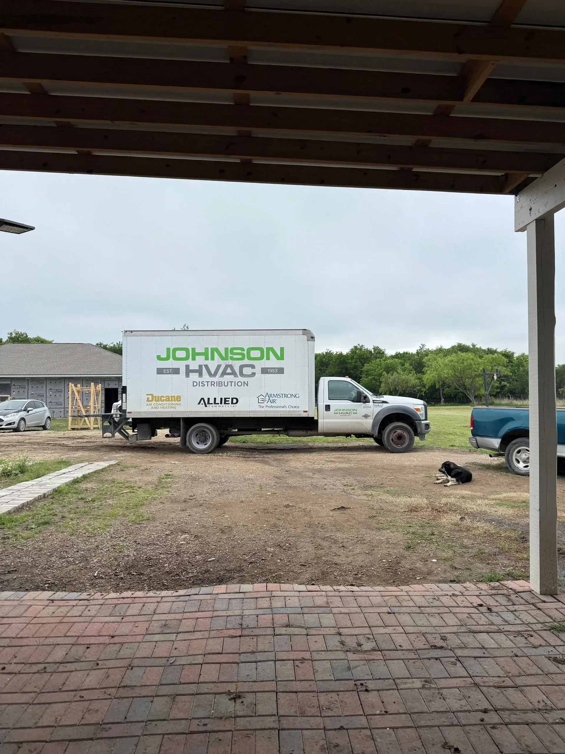 White Johnson Moving truck parked on gravel under a carport, with a brick patio in the foreground.