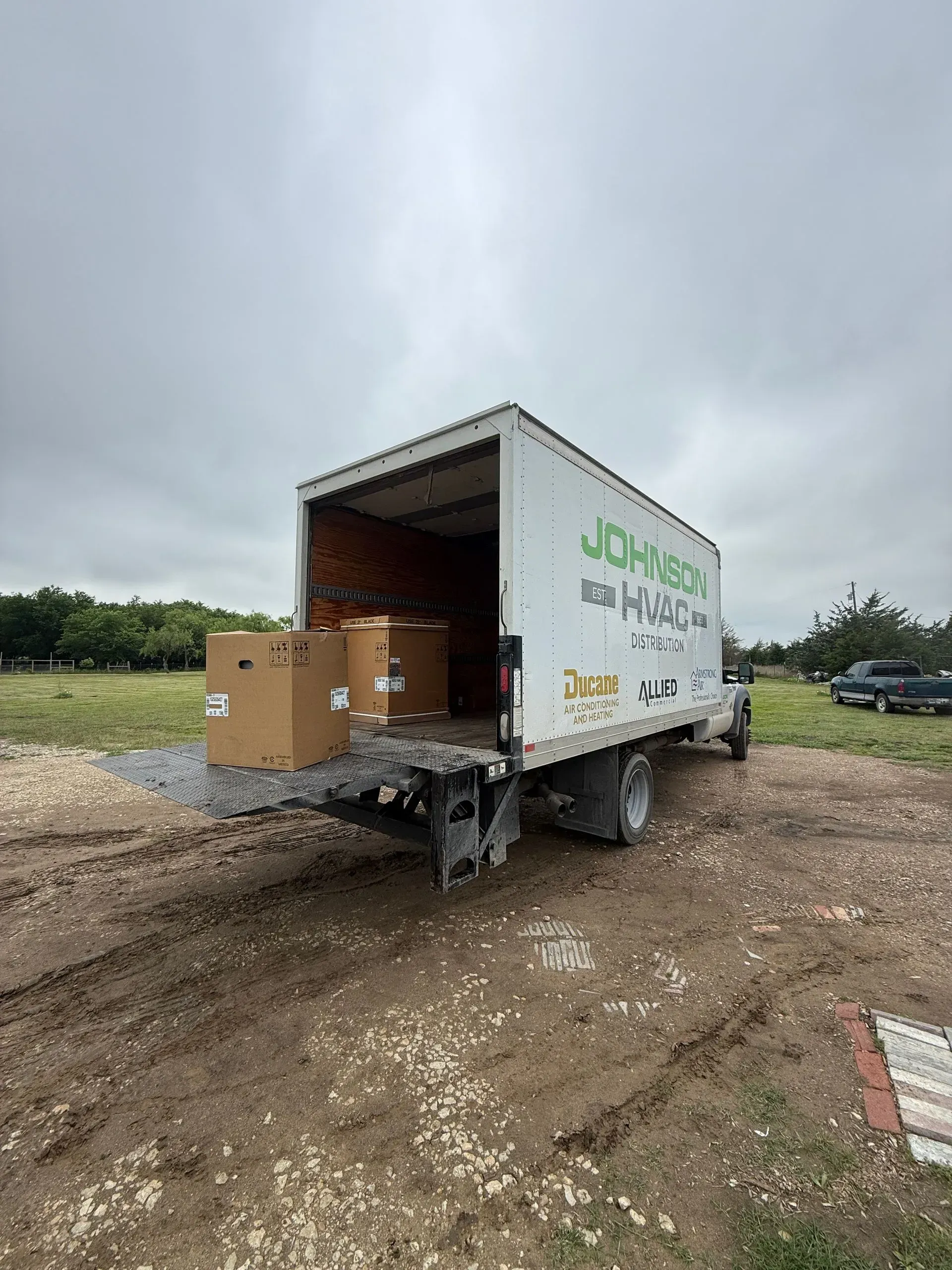 White moving truck on a muddy lot with rear cargo door open and boxes inside, under cloudy skies