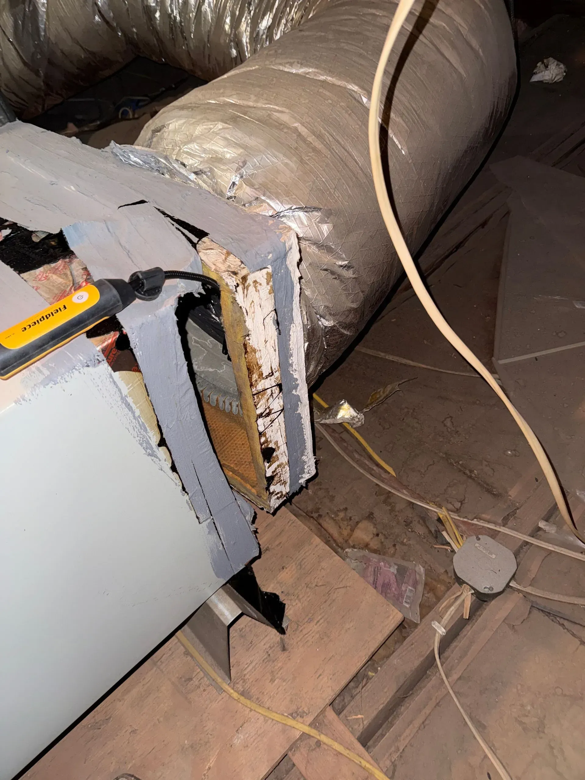 Damaged HVAC ducting in an attic, with torn insulation and loose wires on the floor.
