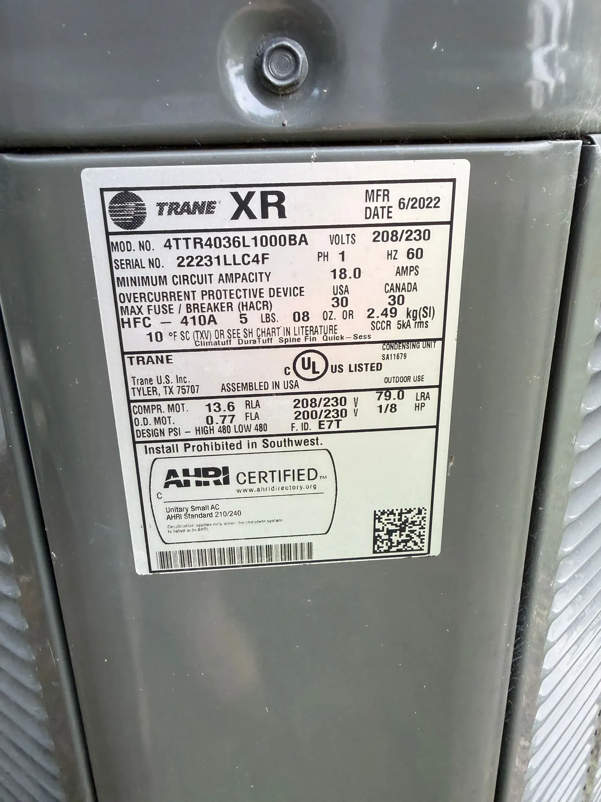 Close-up of a gray appliance data label with small black text and logos on a metal surface.