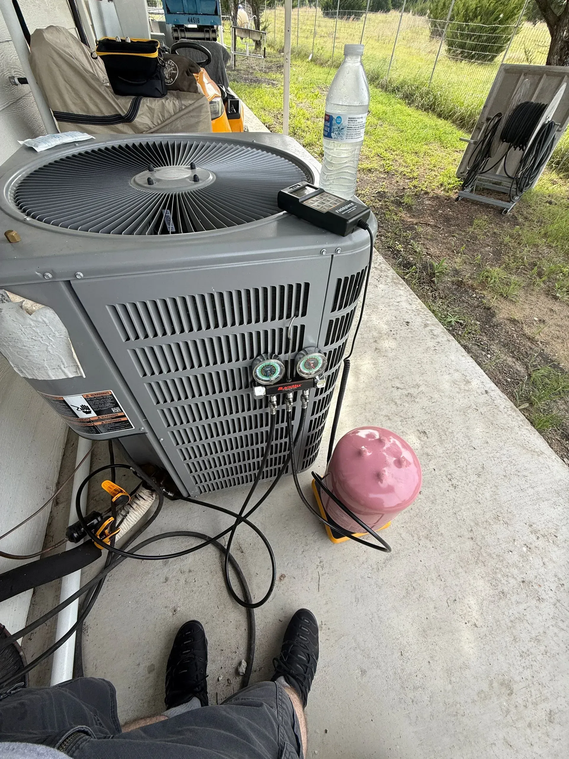 Outdoor view of a gray air conditioner unit beside a pink ball and tangled cords on a concrete patio