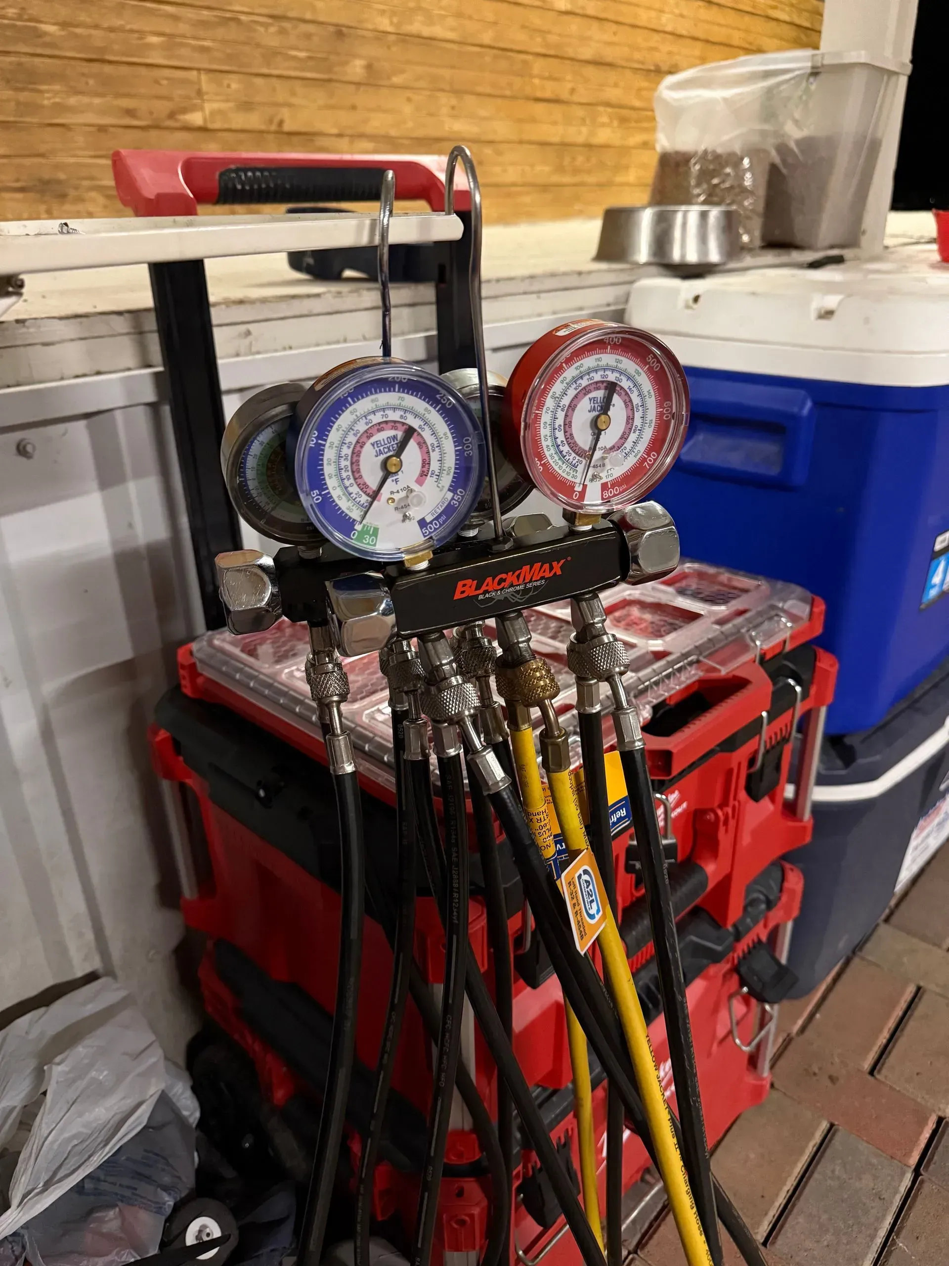 Two pressure gauges and hoses on a red tool case beside a blue cooler in a garage.