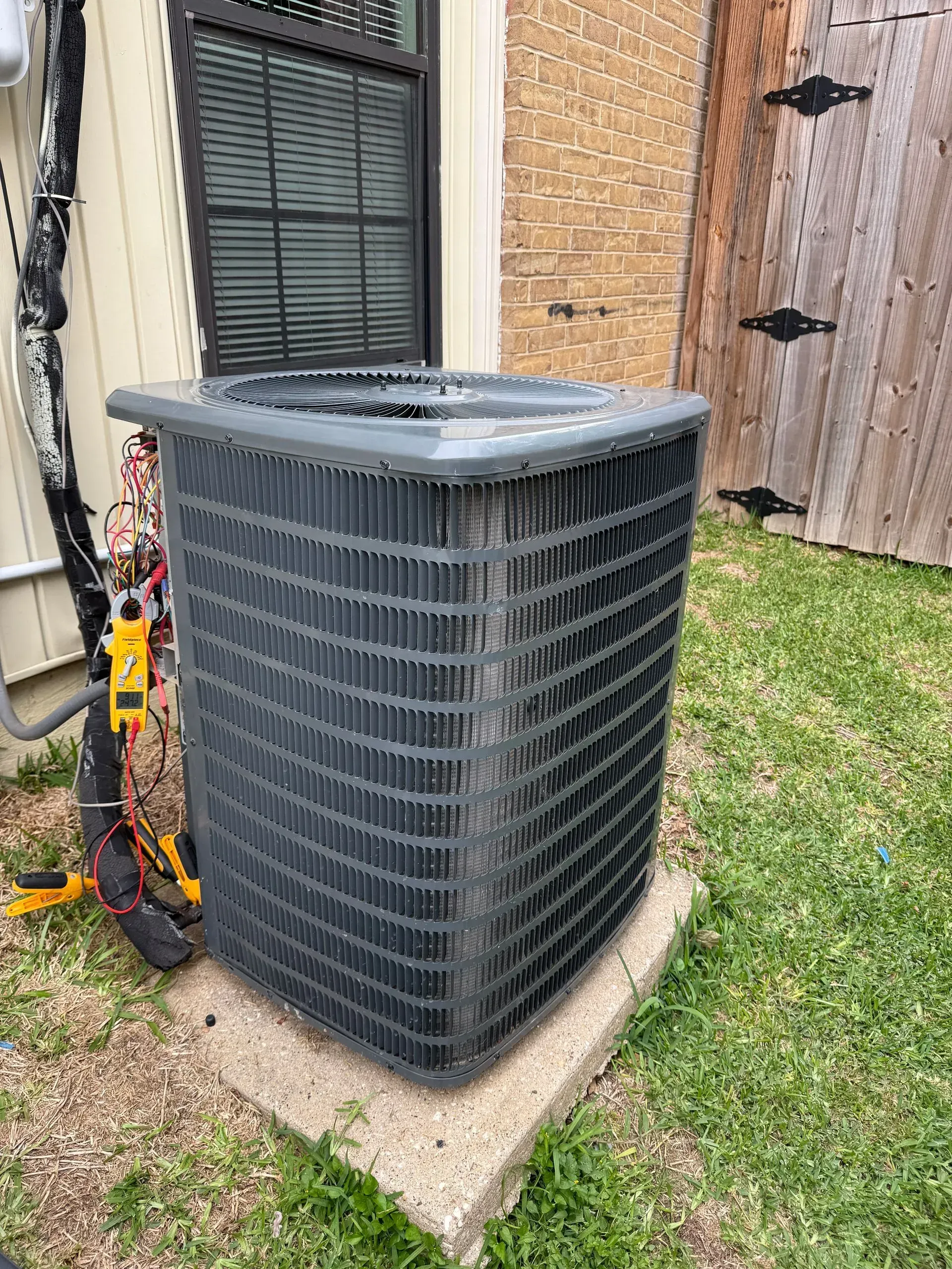 Outdoor HVAC condenser unit beside a house, on a concrete pad next to a window and grass.