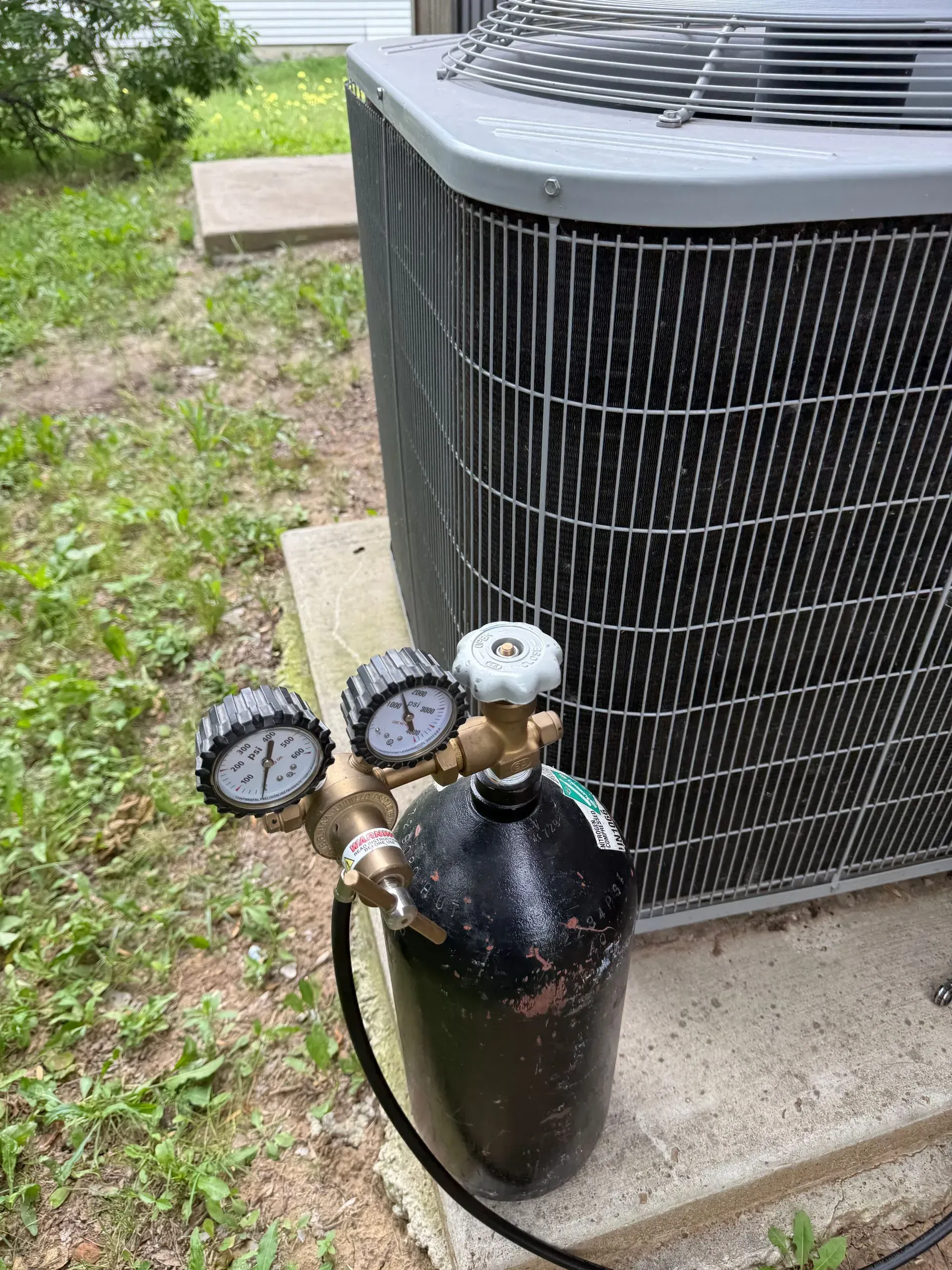 Gas tank with pressure gauges beside a large outdoor air conditioning unit.