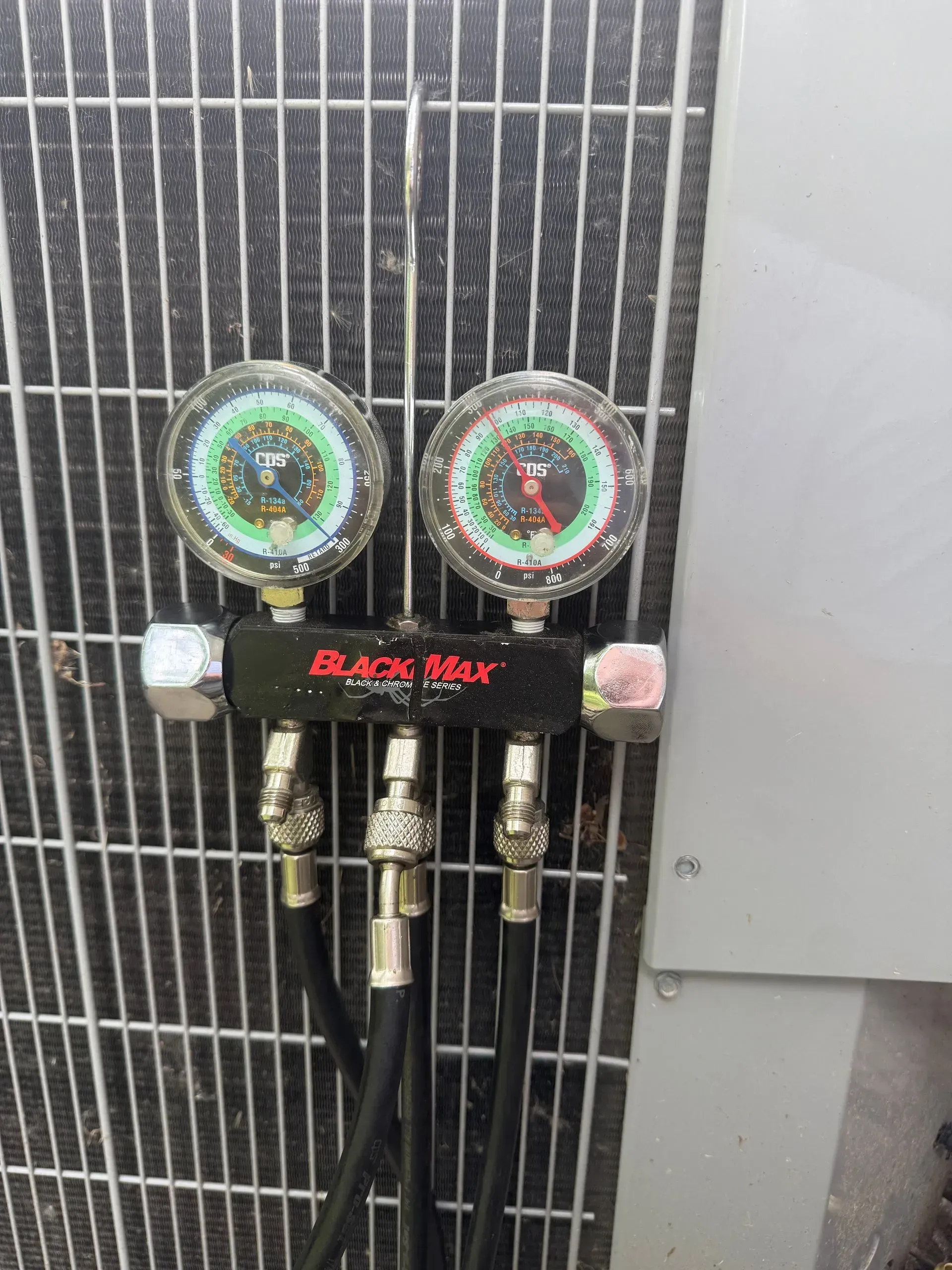 Two HVAC gauges and valves attached to a gray outdoor air conditioning unit