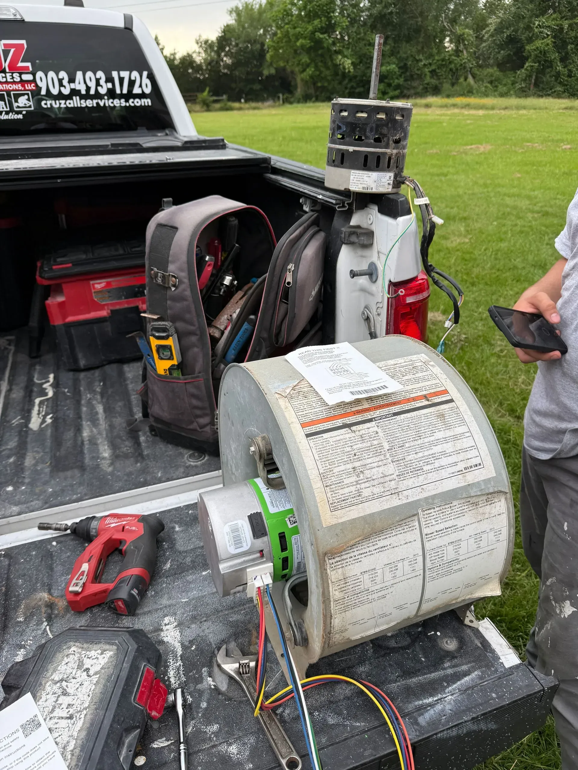 Tools and equipment in a truck bed beside a person holding a phone outdoors