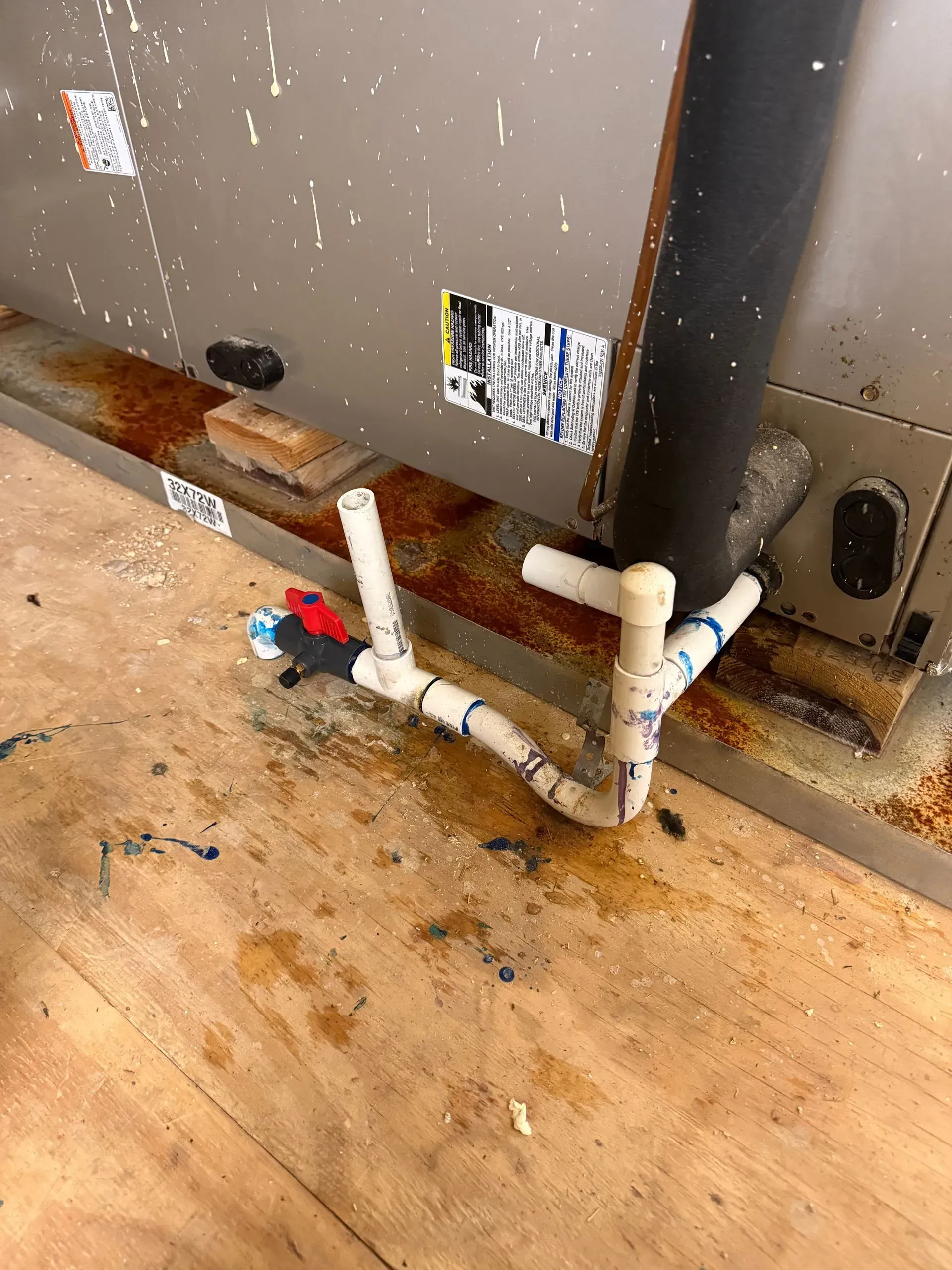 PVC pipes and valves on a dirty floor beside a gray utility appliance