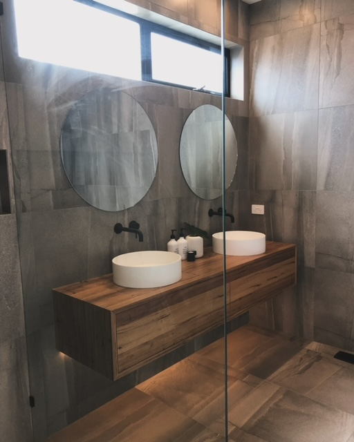 Modern bathroom with floating wood vanity, round mirrors, vessel sinks, and glass shower partition