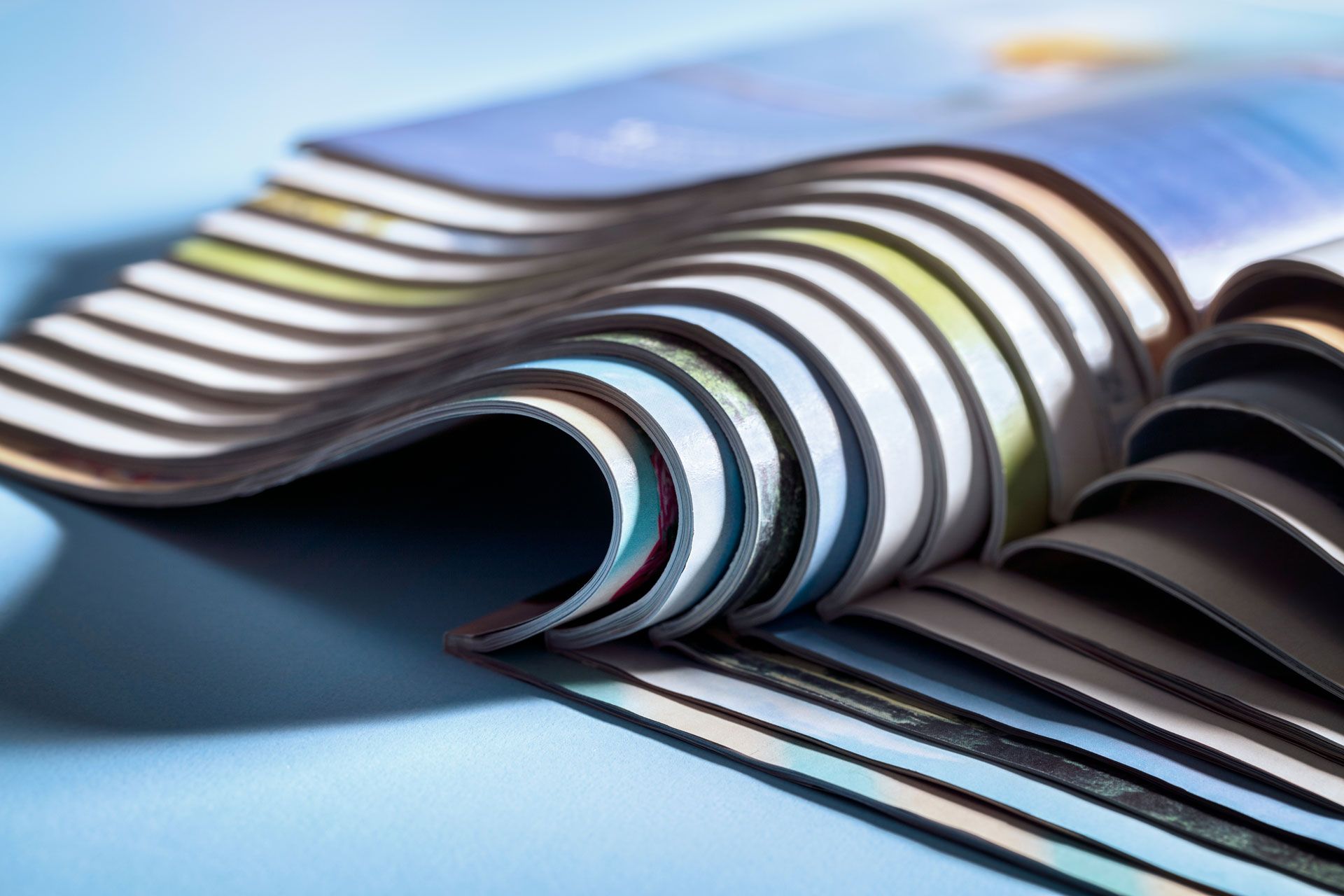 Stacked pages of a magazine or brochure fanned out against a soft blue background, showing layered edges.