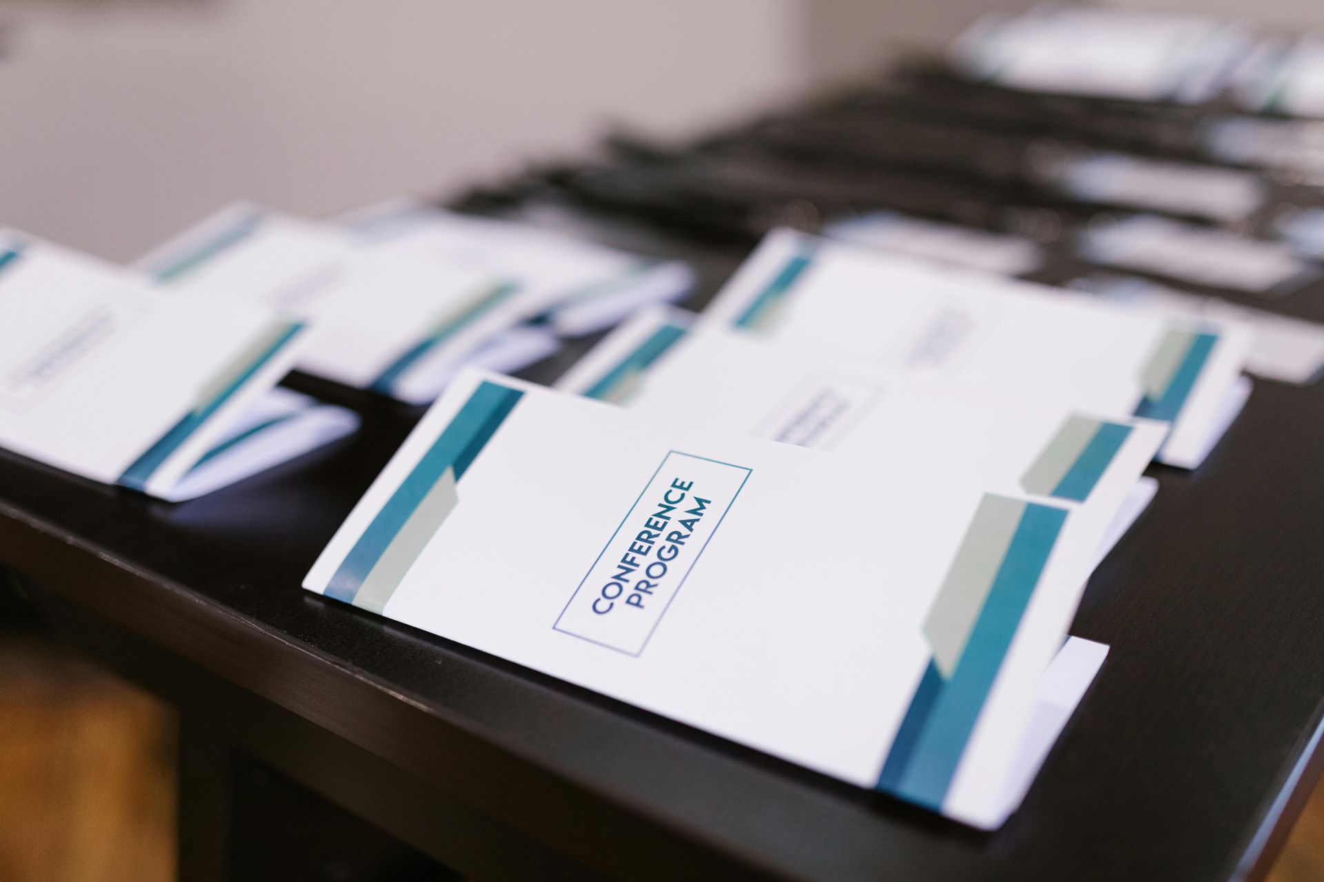 Several white conference programs with blue and grey accents arranged on a black table.