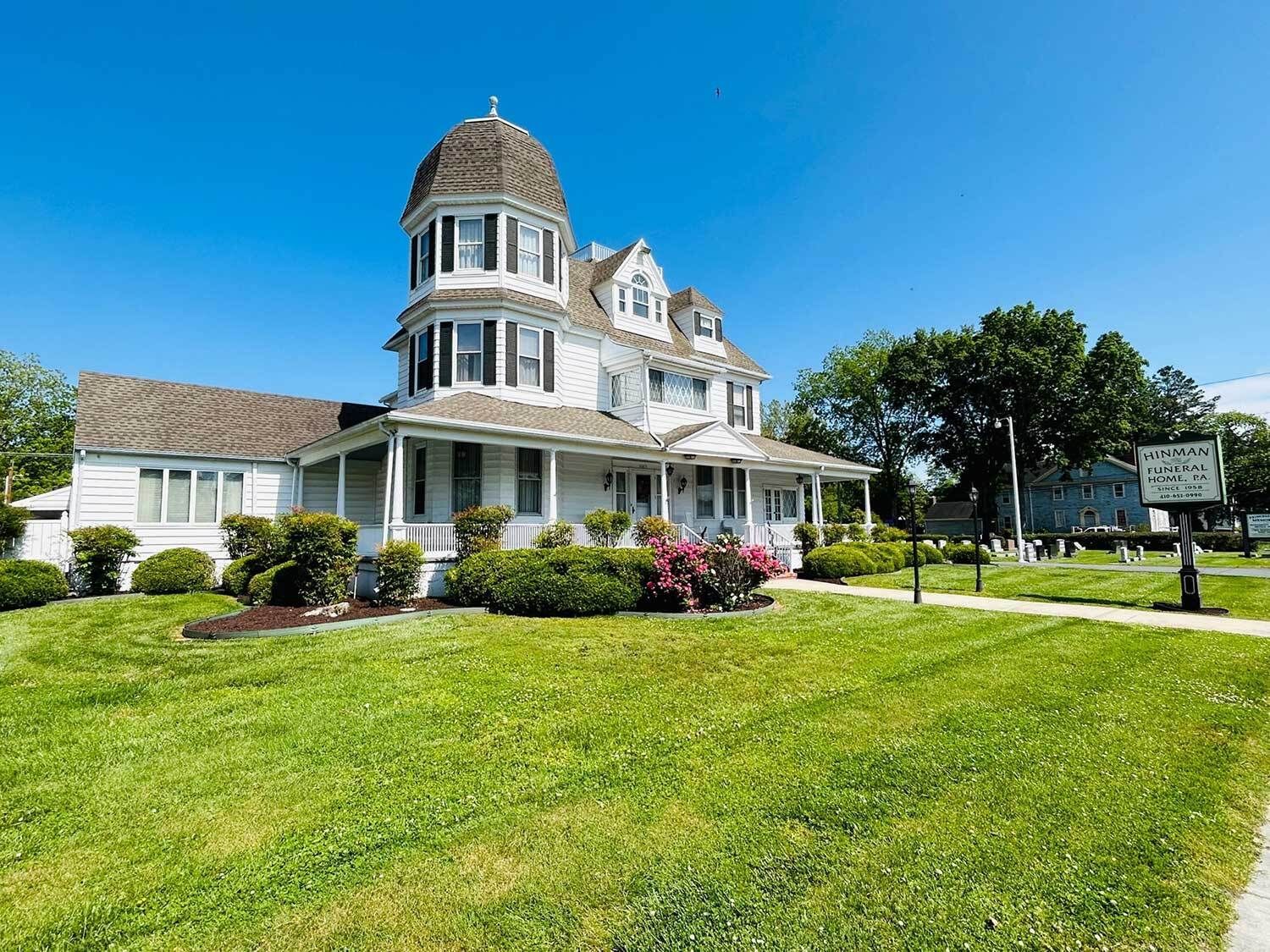 White Victorian house with a domed turret, green lawn, and blue sky.