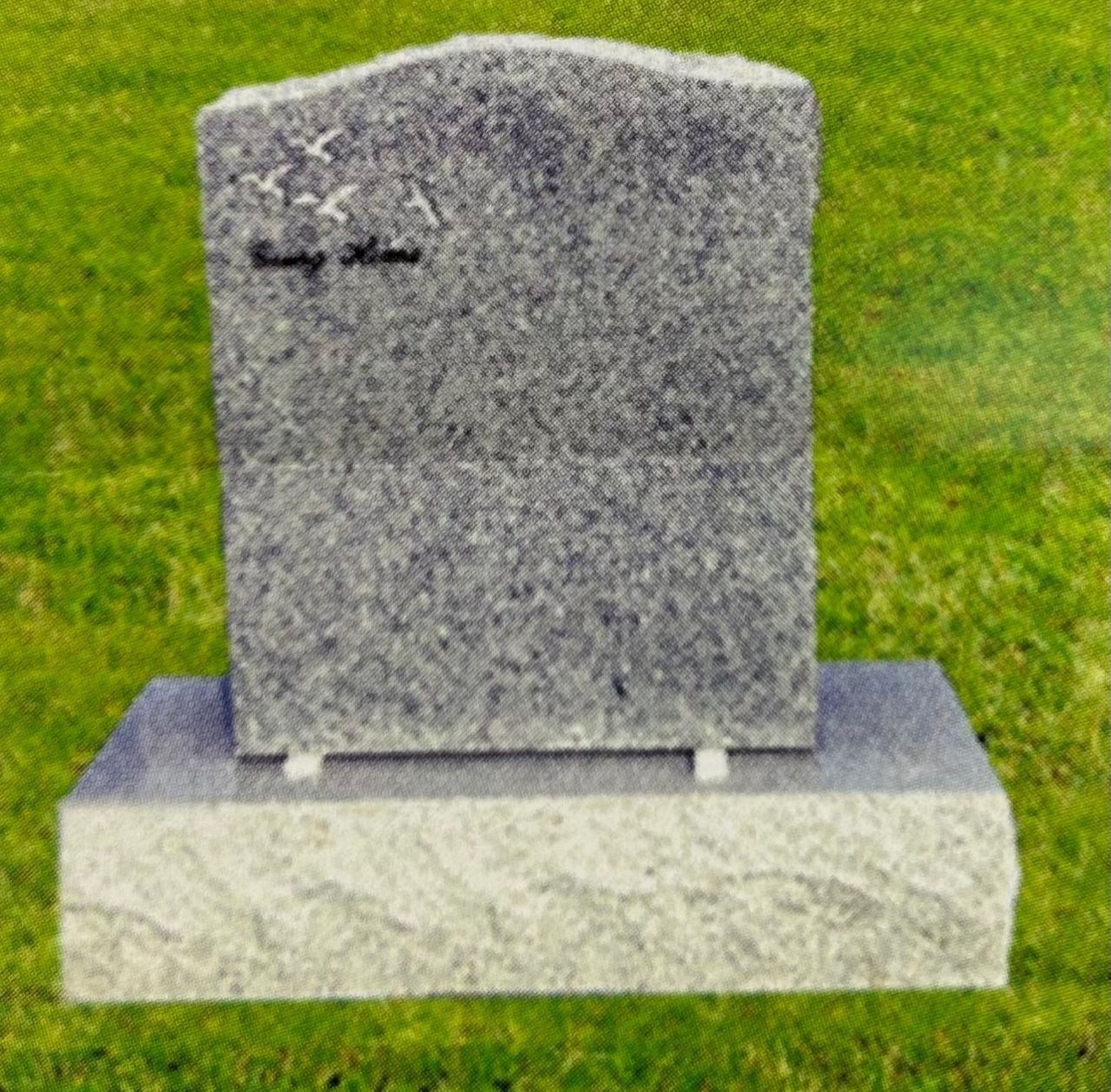 Granite headstone with flying bird engraving, set on a stone base, placed on green grass.
