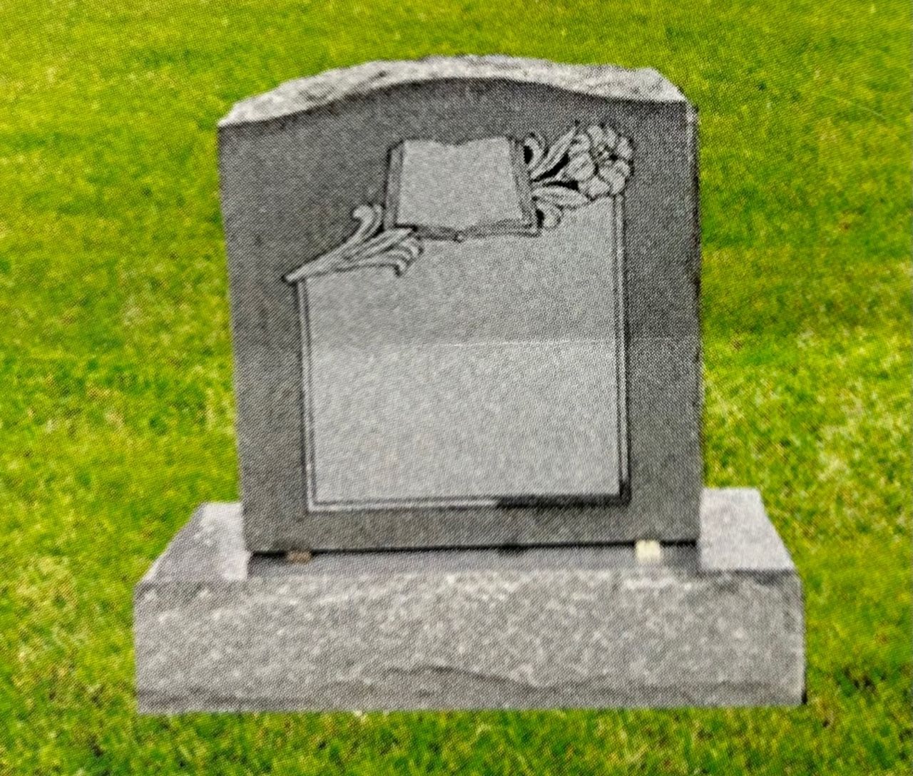 Gray granite headstone with decorative floral design against green grass.