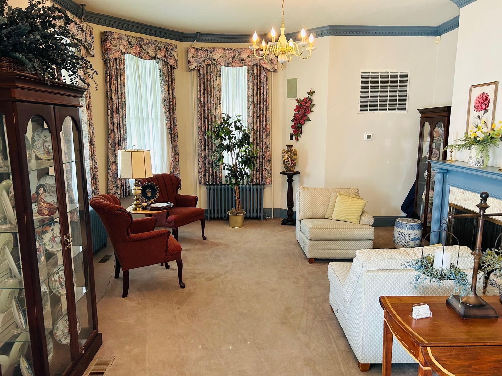 Living room with antique furniture, floral curtains, and a chandelier.