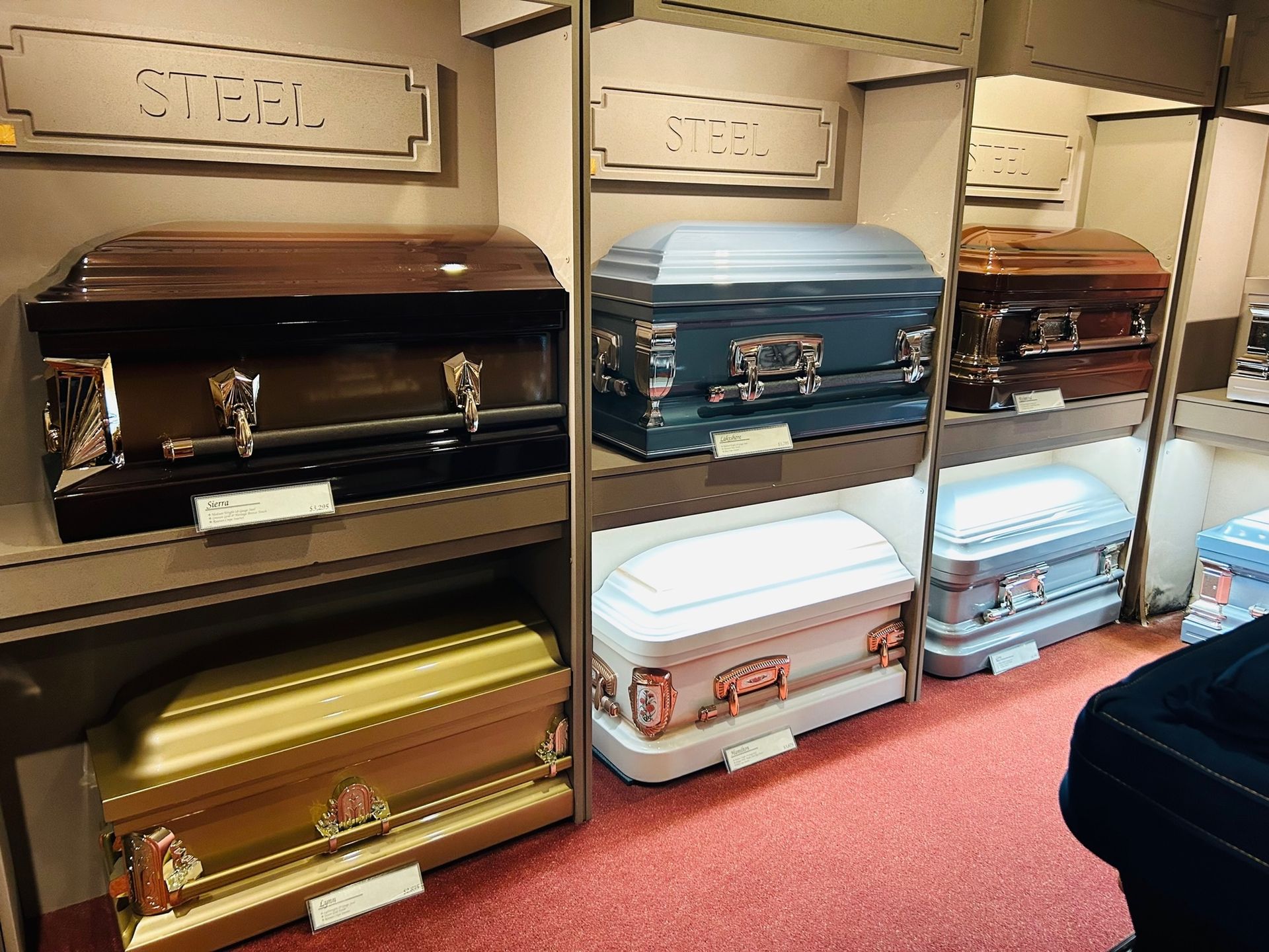 Caskets displayed on shelves in a showroom, varying colors and styles.
