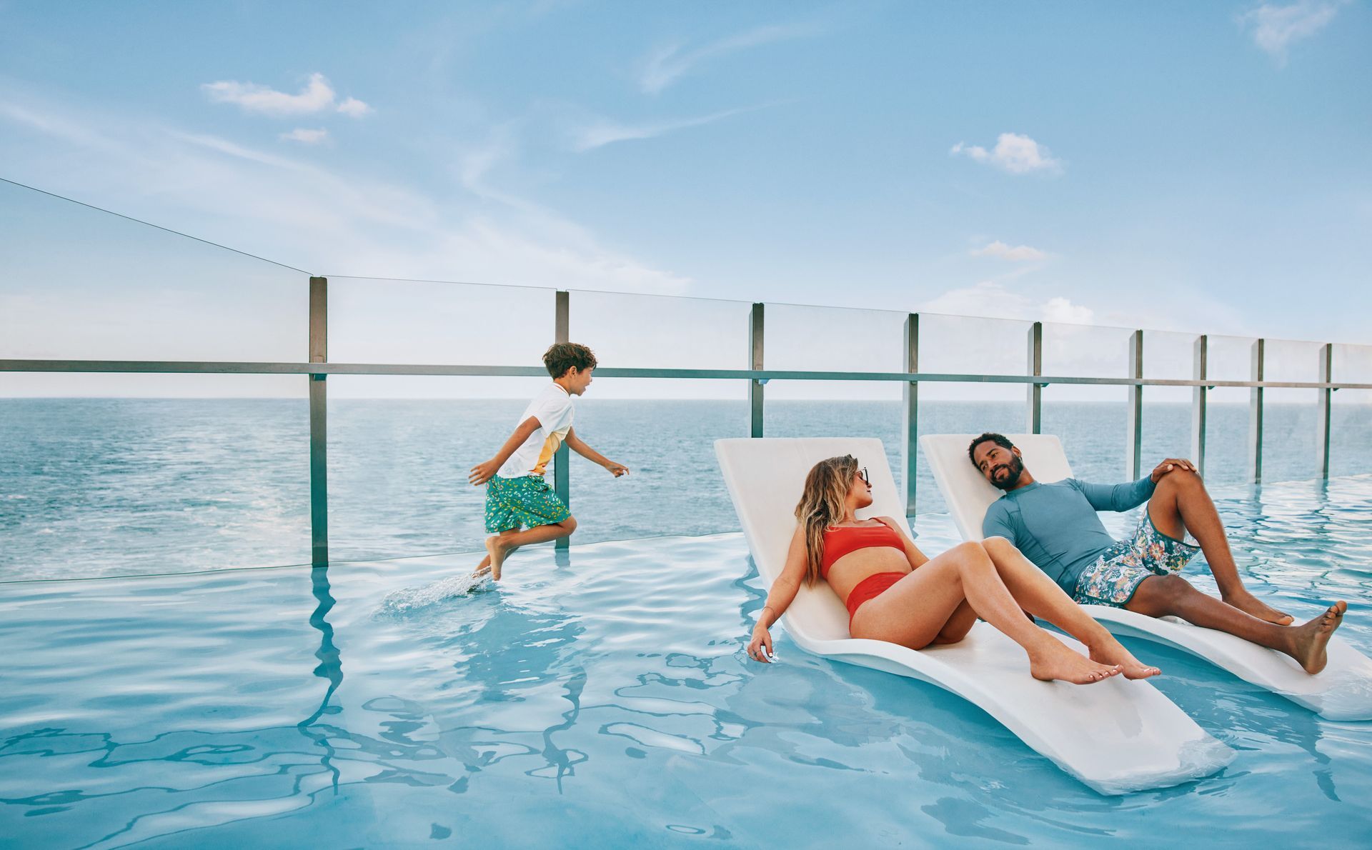 Three people relax in a rooftop infinity pool with lounge chairs and ocean views.