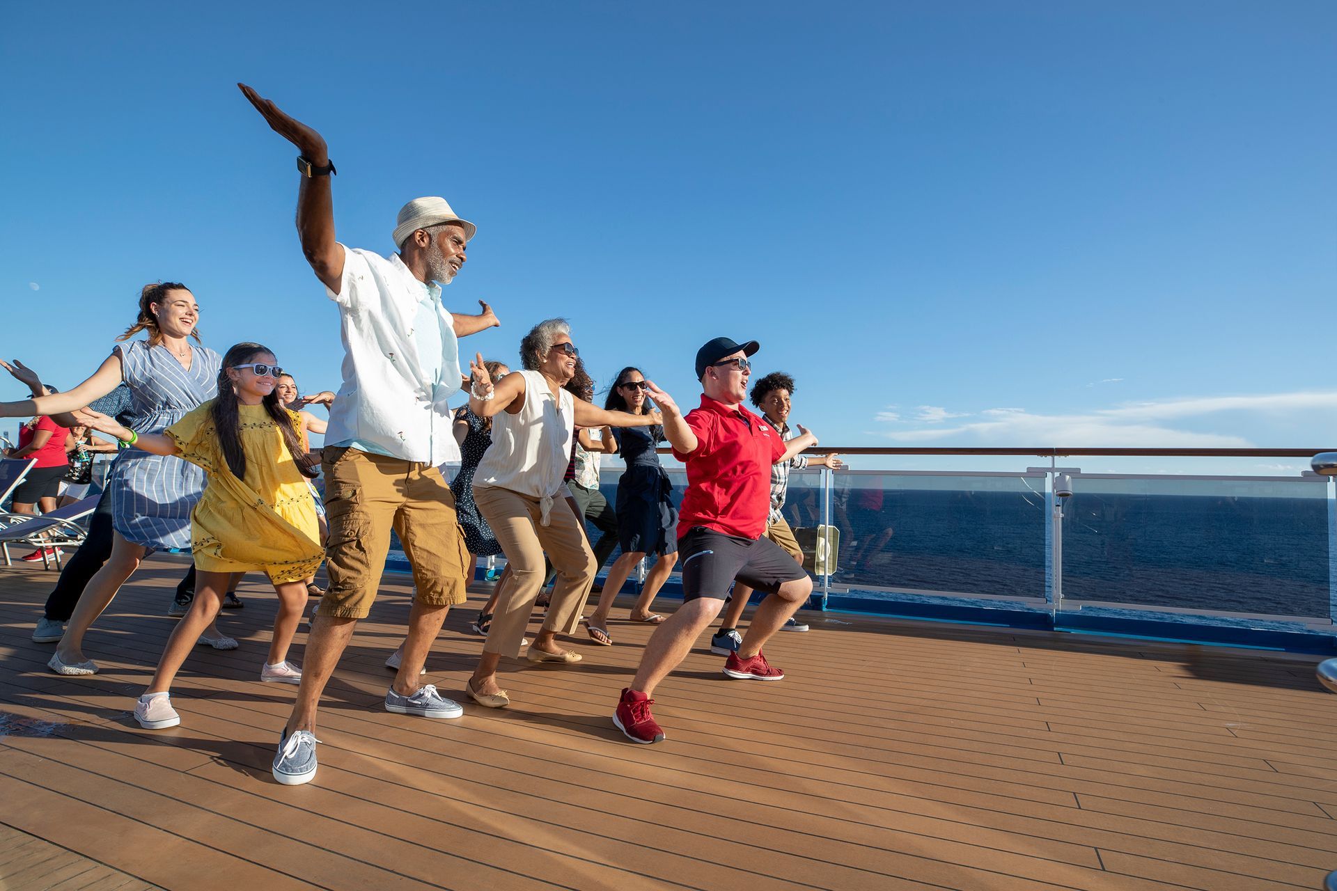 Group dancing on a ship deck under a clear blue sky, with ocean and railing in the background