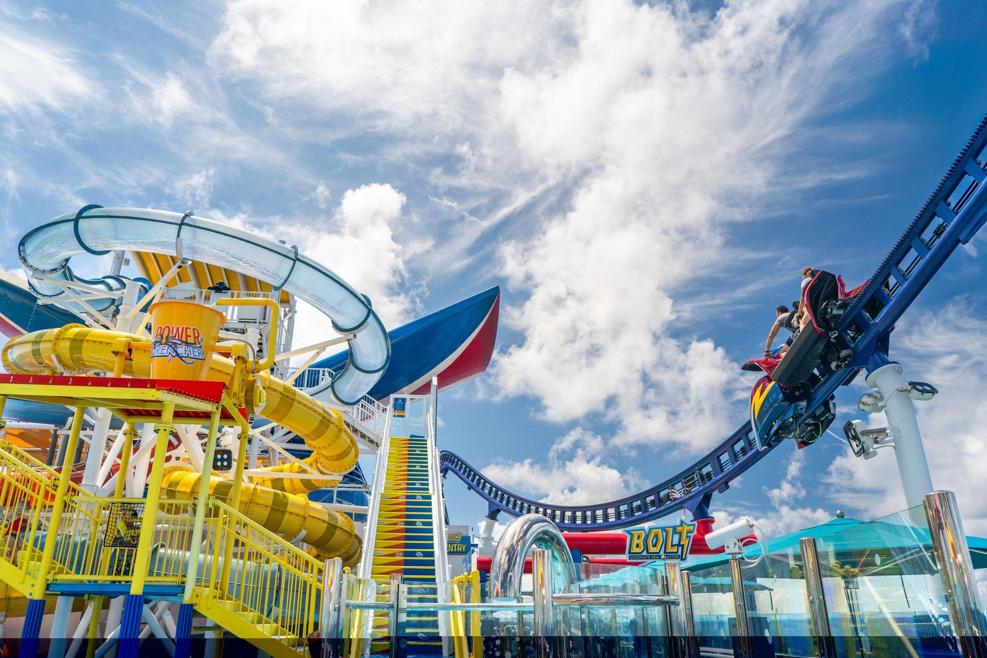 Amusement park with bright yellow and blue rides under a cloudy sky, with riders on a blue coaster track.