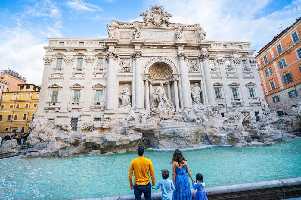 Trevi Fountain in Rome with turquoise water and three people viewing it from the edge