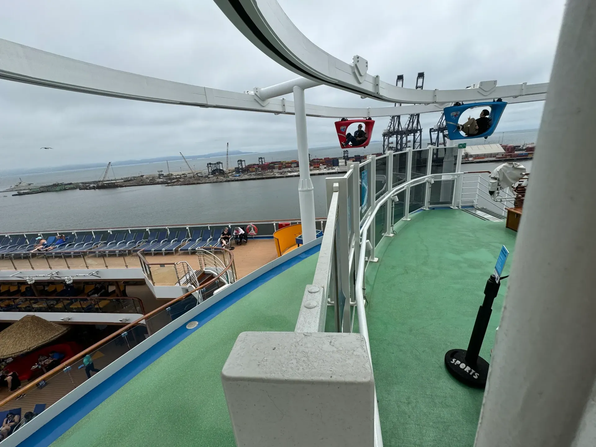 View from a cruise ship deck with ocean, lifeboat, and railings under a cloudy sky