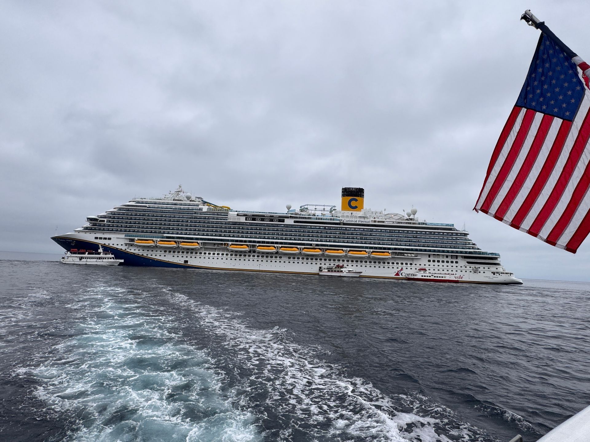 Large cruise ship at sea, viewed from behind with an American flag in the foreground