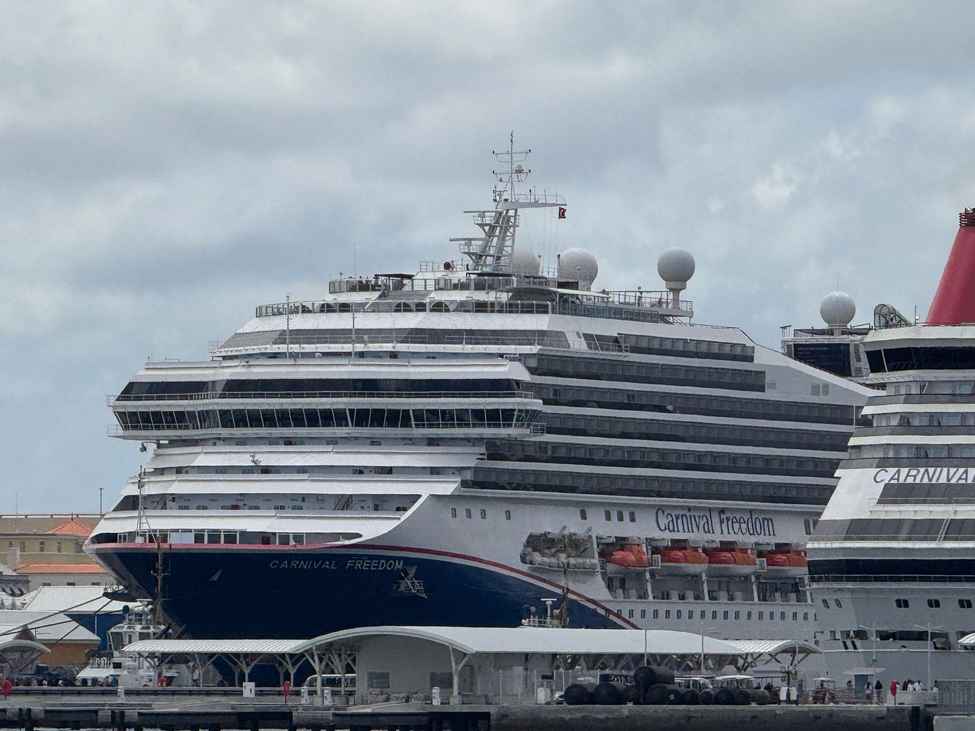 Two large cruise ships docked at a port under a cloudy sky