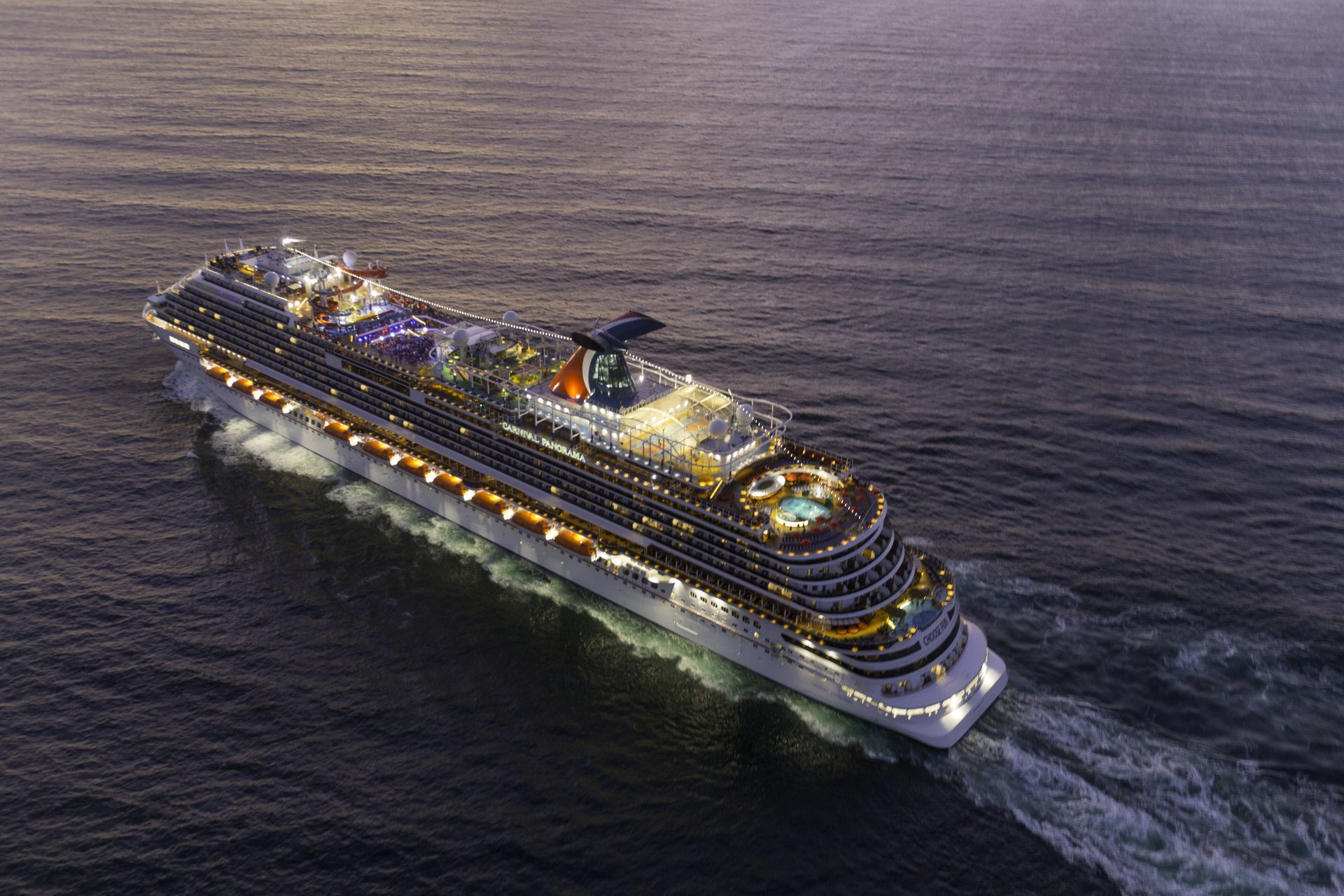 Large illuminated cruise ship sailing at night on dark open water.