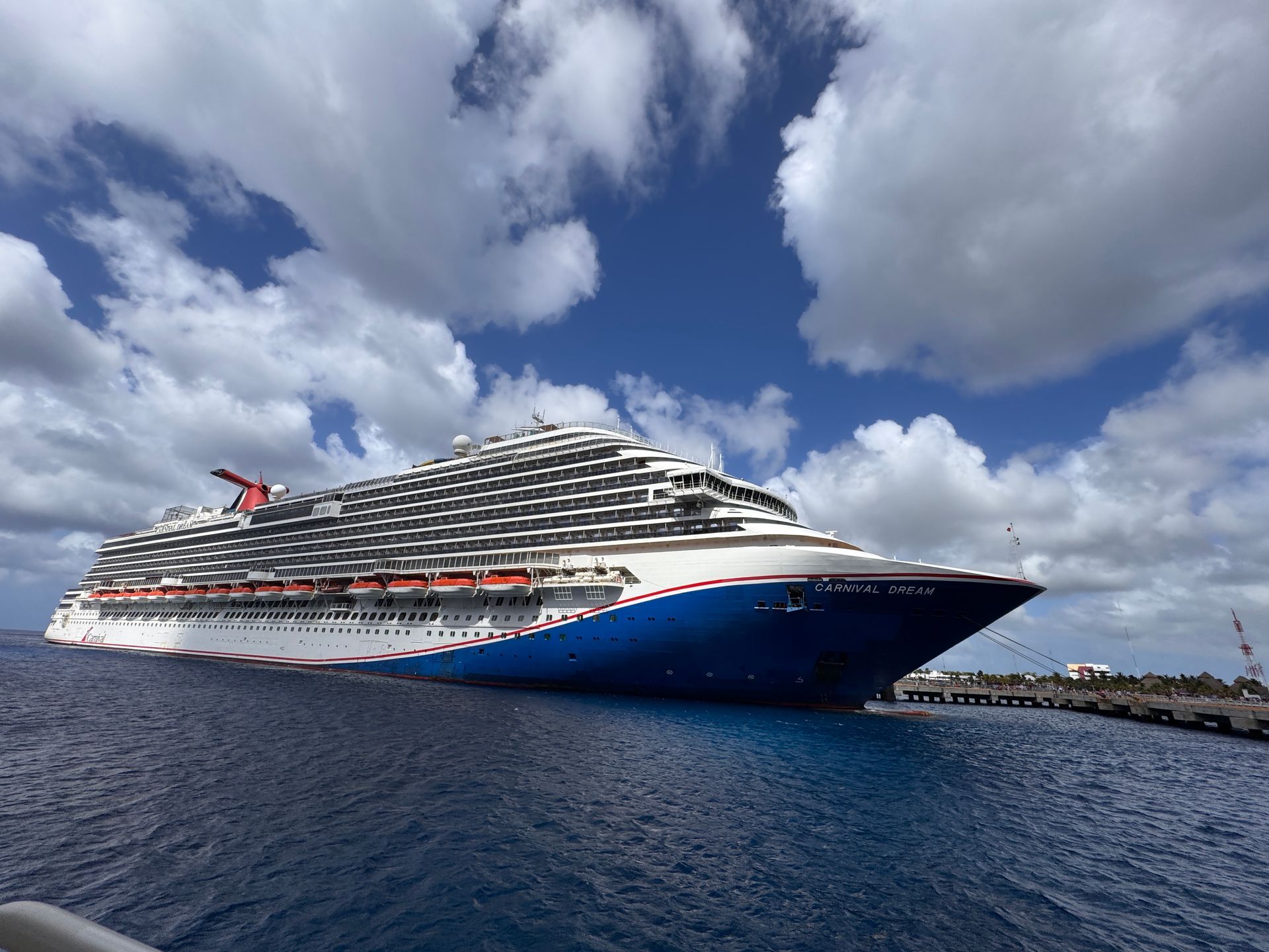 Large white cruise ship with a blue bow sailing on calm water under cloudy blue sky