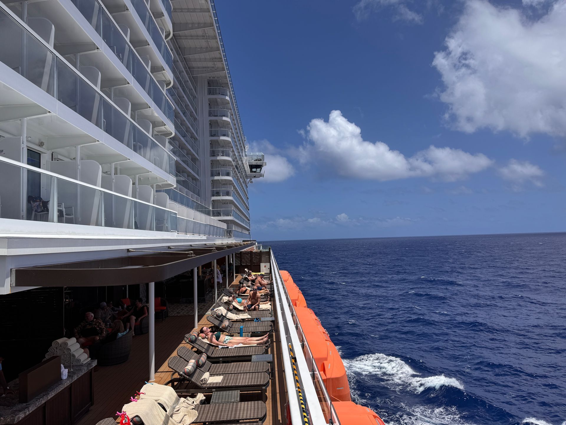 Cruise ship deck with lounge chairs beside the blue ocean under a sunny sky