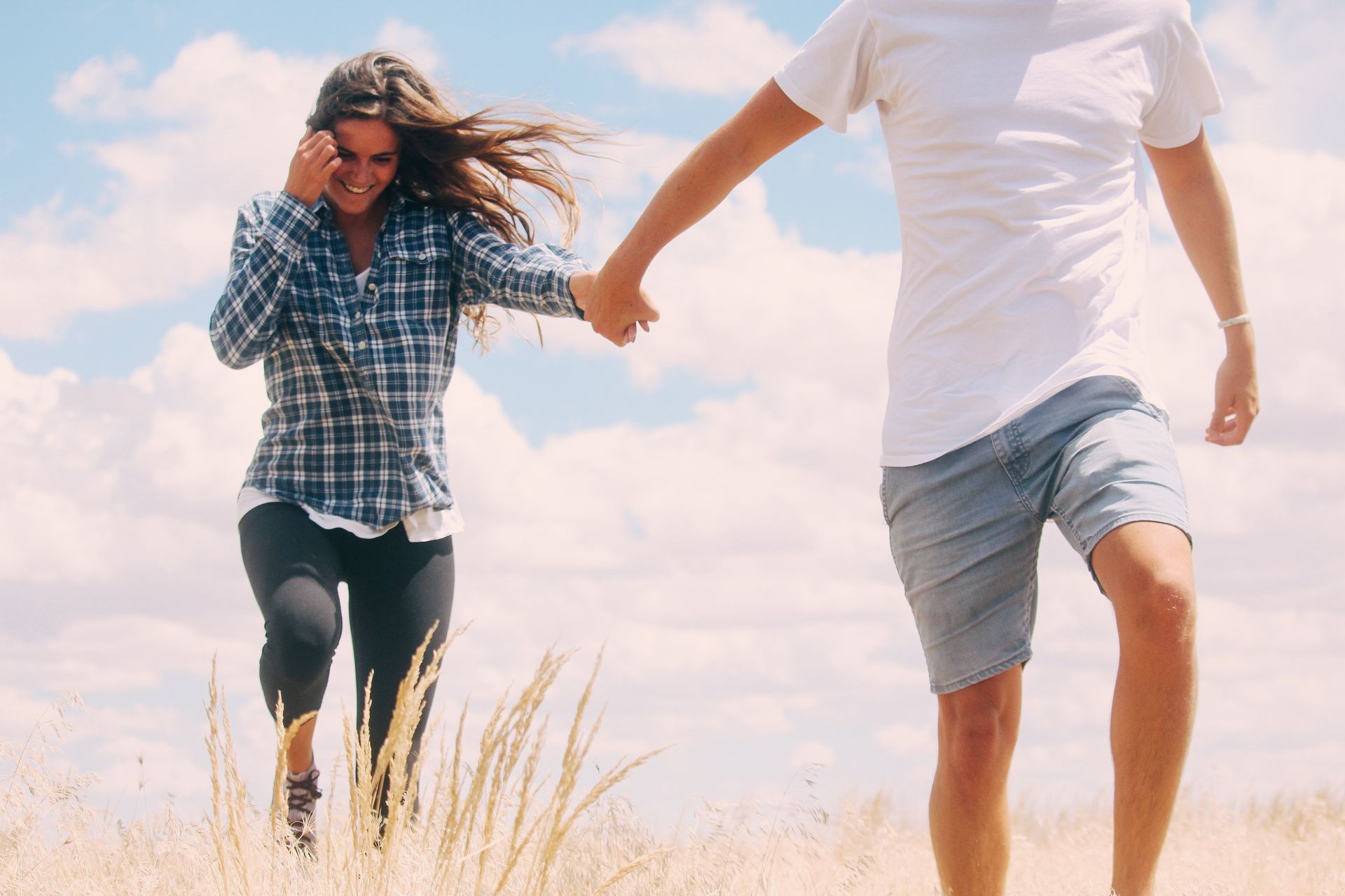 Two people running hand in hand through a sunny field under a blue sky